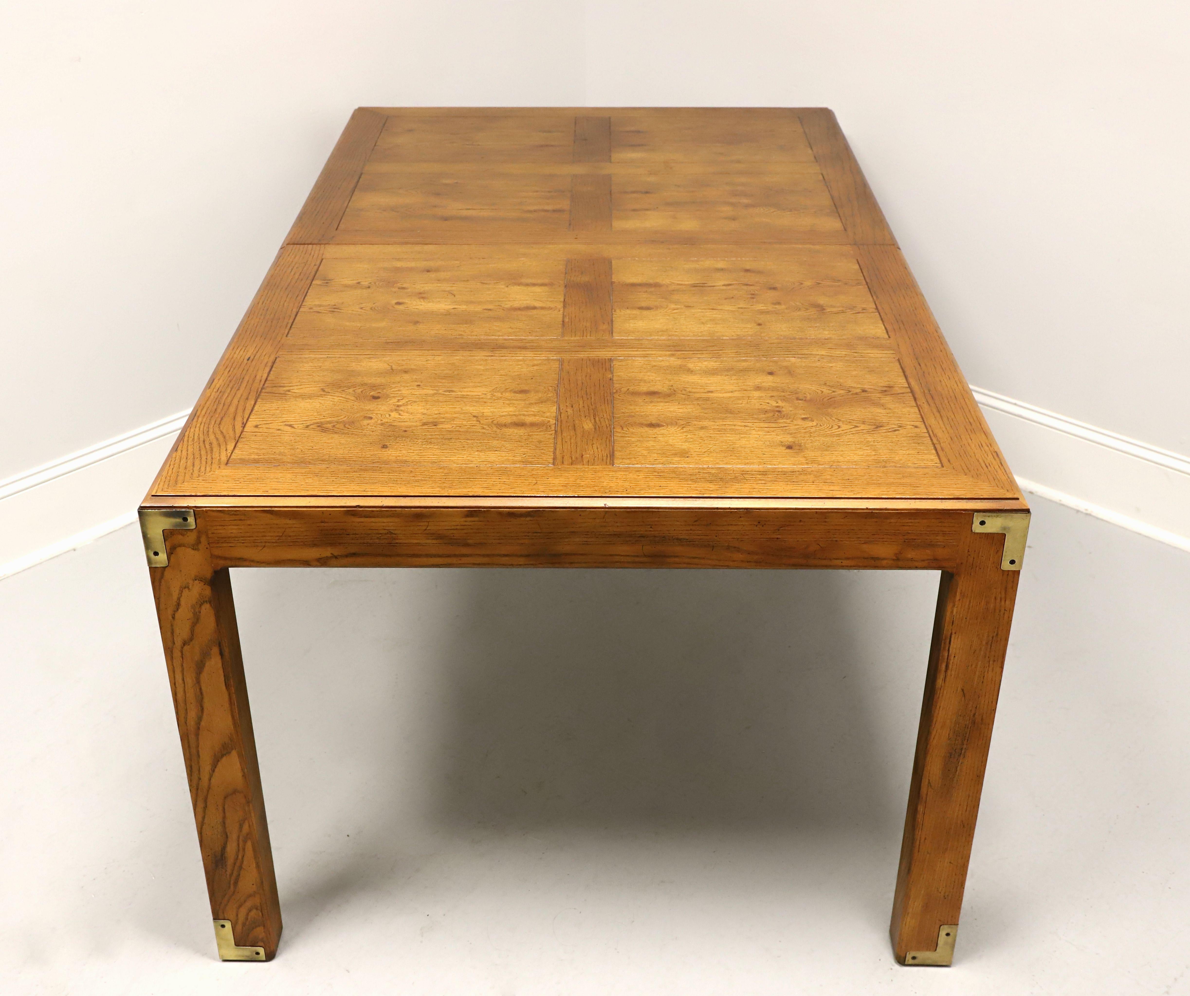 A campaign style dining table by Henredon, from their Artefacts Collection. Knotty oak with a slightly distressed finish, banded beveled edge top with a parquetry pattern, brass accents to corners & feet, full apron, and square straight legs.