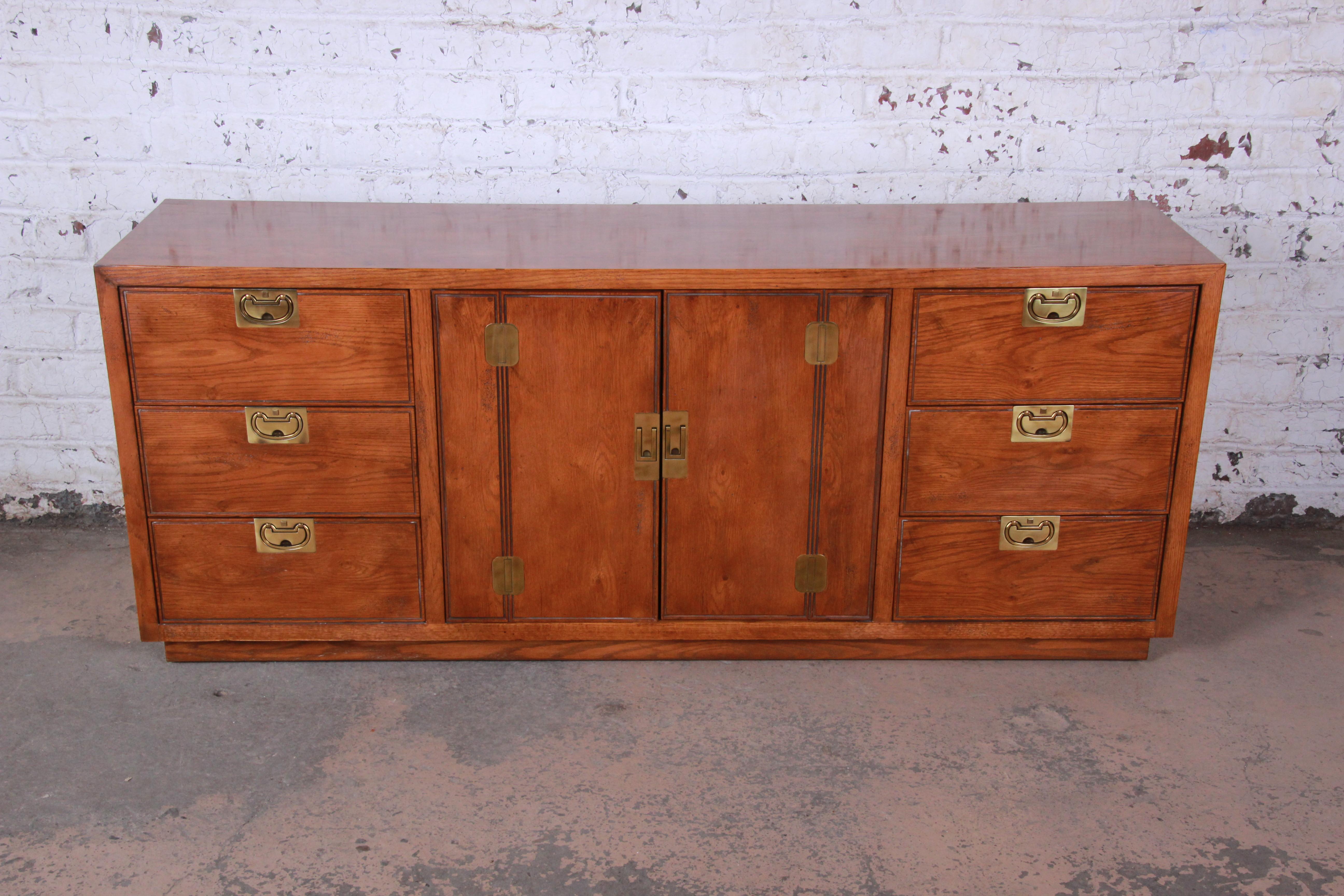 Offering a very nice Henredon Campaign style oak long dresser or credenza from the Bel Air line. The piece offers an ample amount of storage with the two centre cabinet doors opening up to a shelf for storage. On each side of the cabinet doors are