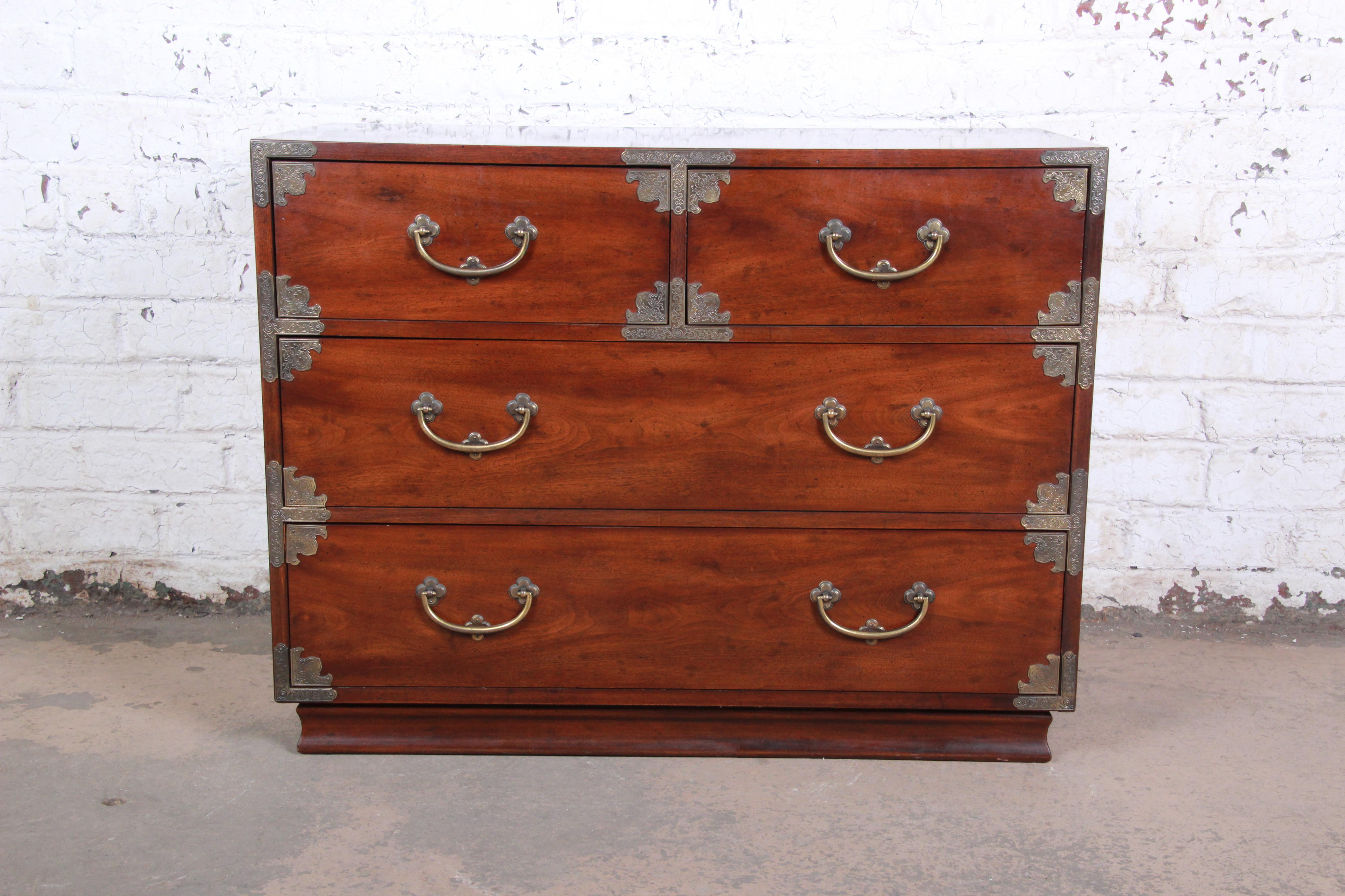 An exceptional Hollywood Regency Campaign style chest of drawers by Henredon. The dresser features stunning walnut wood grain, with original Asian-inspired brass hardware and accents. It offers ample storage, with four deep dovetailed drawers. The