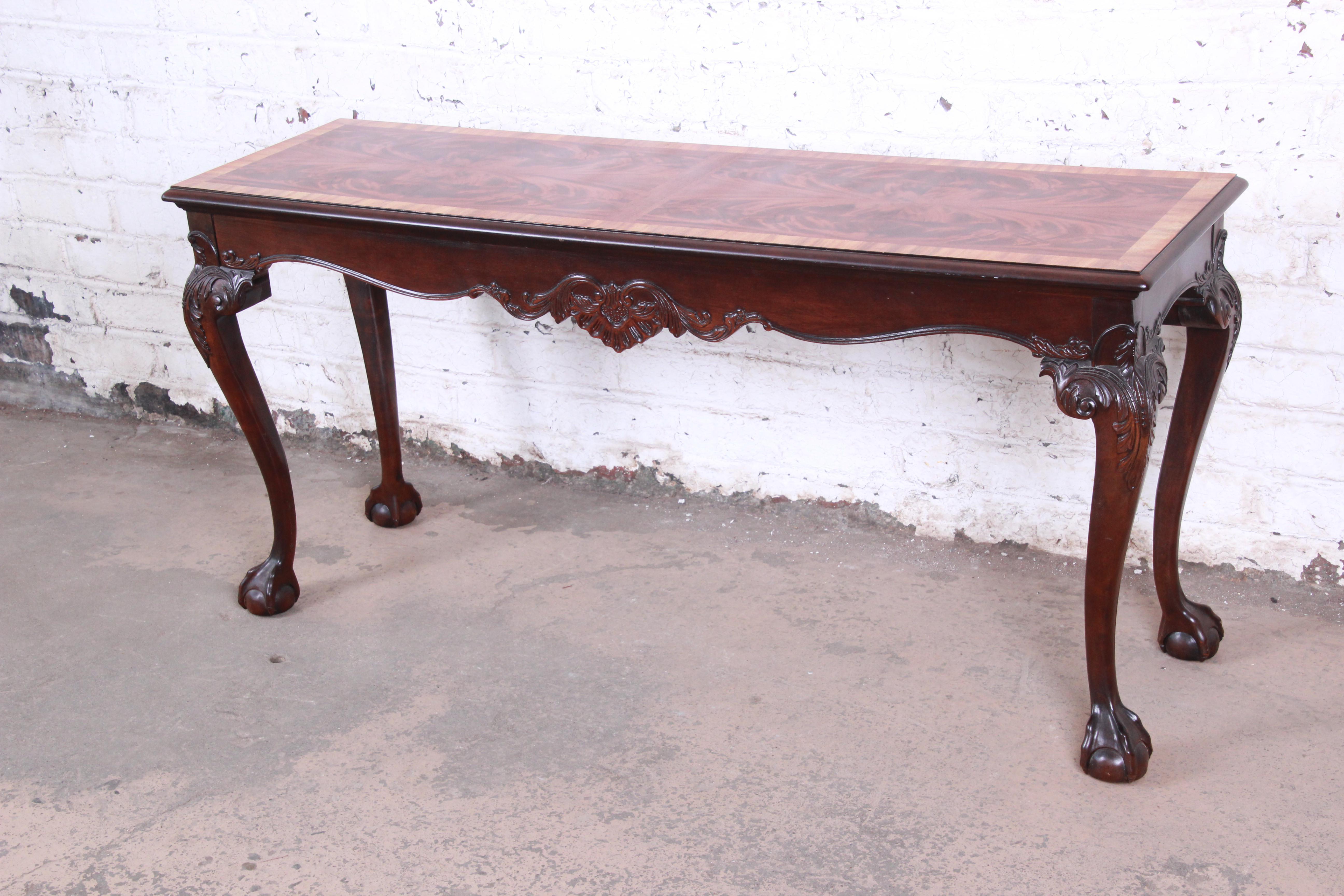 An exceptional Chippendale style carved mahogany console table or sofa table by Henredon. The table features a stunning banded flame mahogany top and gorgeous carved wood details with ball and claw feet. Made with the highest quality craftsmanship,