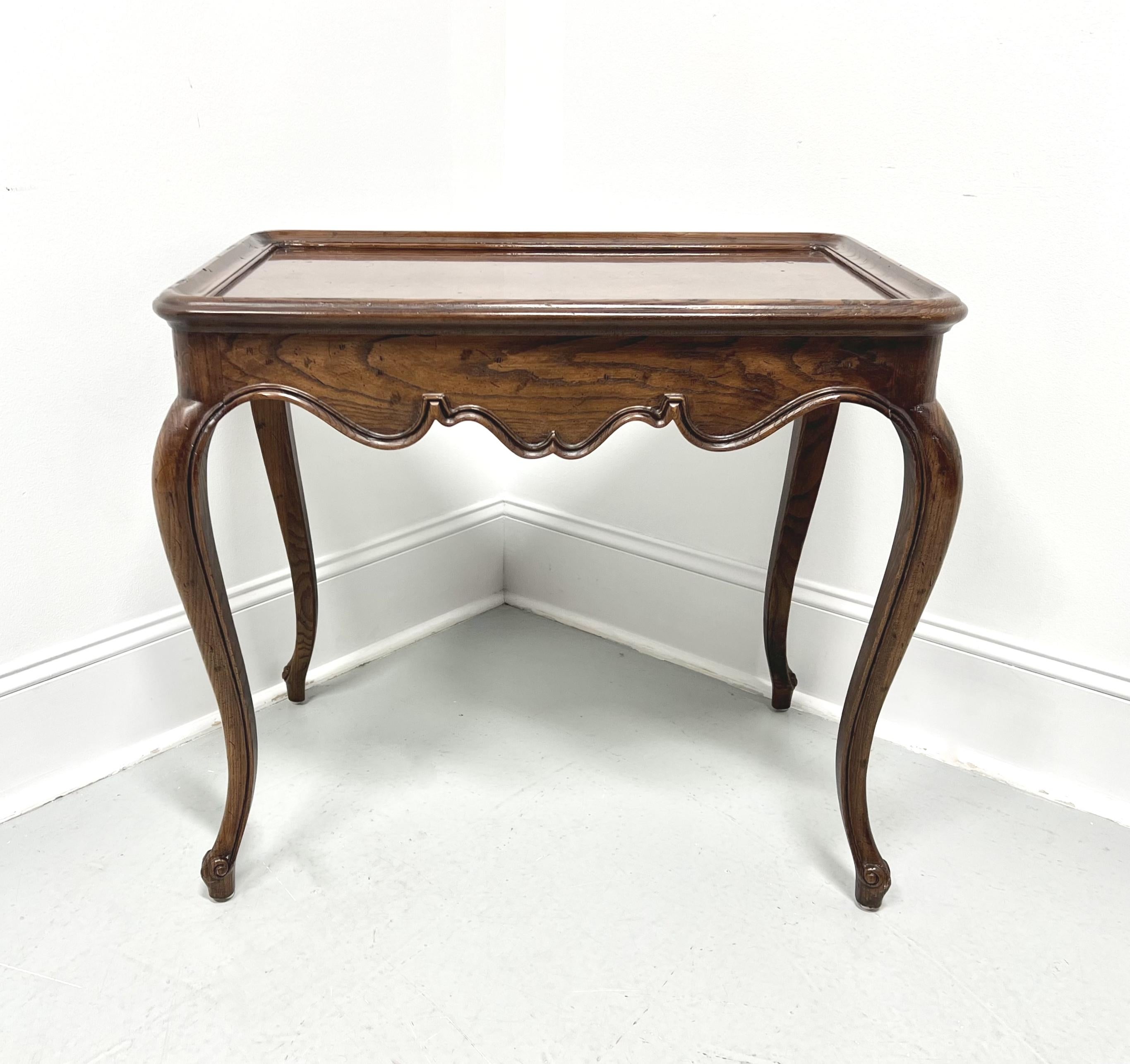 A tea table in the French Country style by Henredon. Burl oak with a distressed finish, bevel edge to the top with rounded corners, two side slide out trays with brass ring pulls, carved apron, curved legs, and scroll feet. Made in Morganton, North
