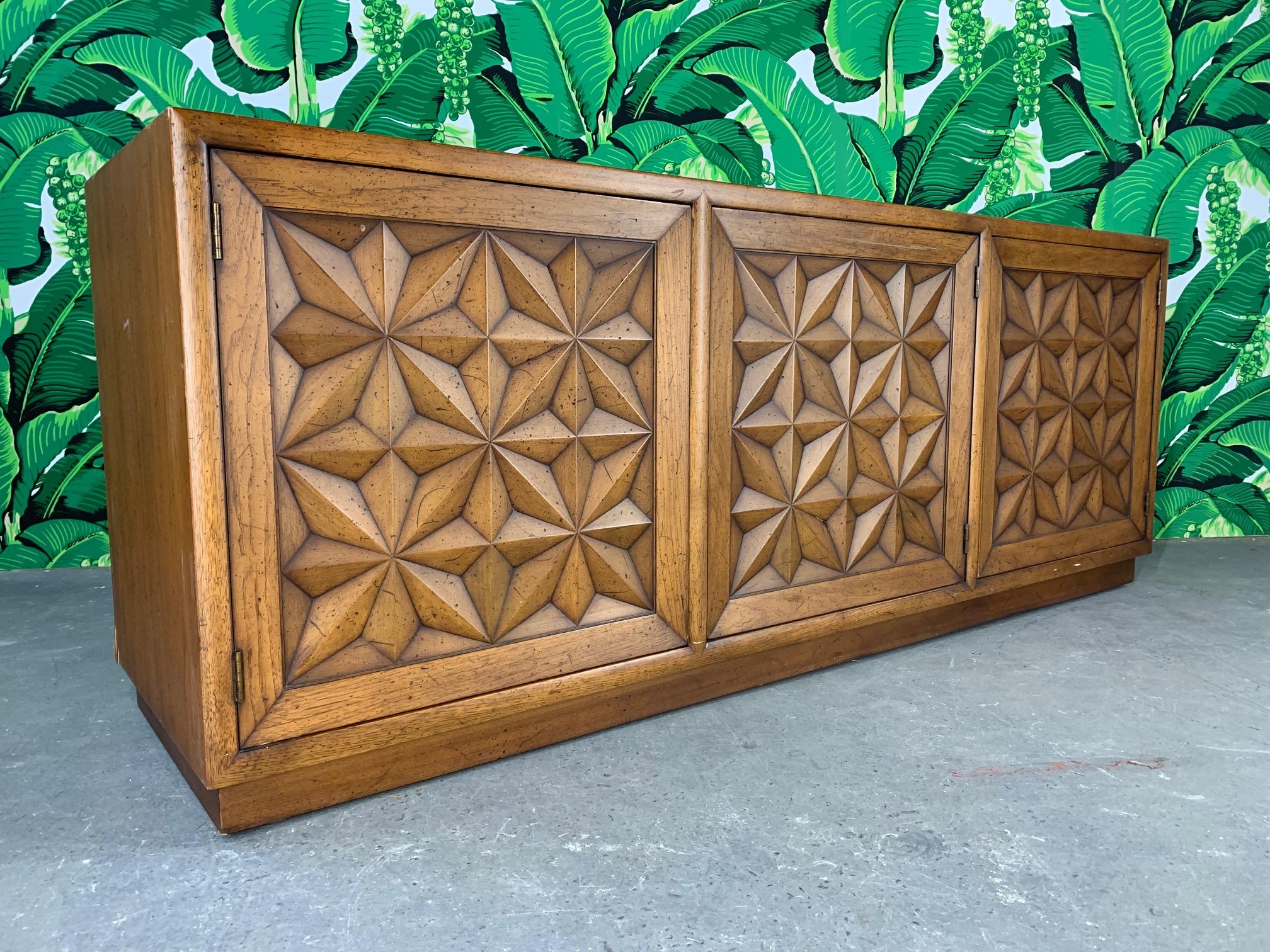 Large credenza by Henredon, part of the Folio Three collection. Features carved door fronts in a striking starburst design and hidden latches (push to open, push to close). Original finish with purposeful distressing, although very slight. Some