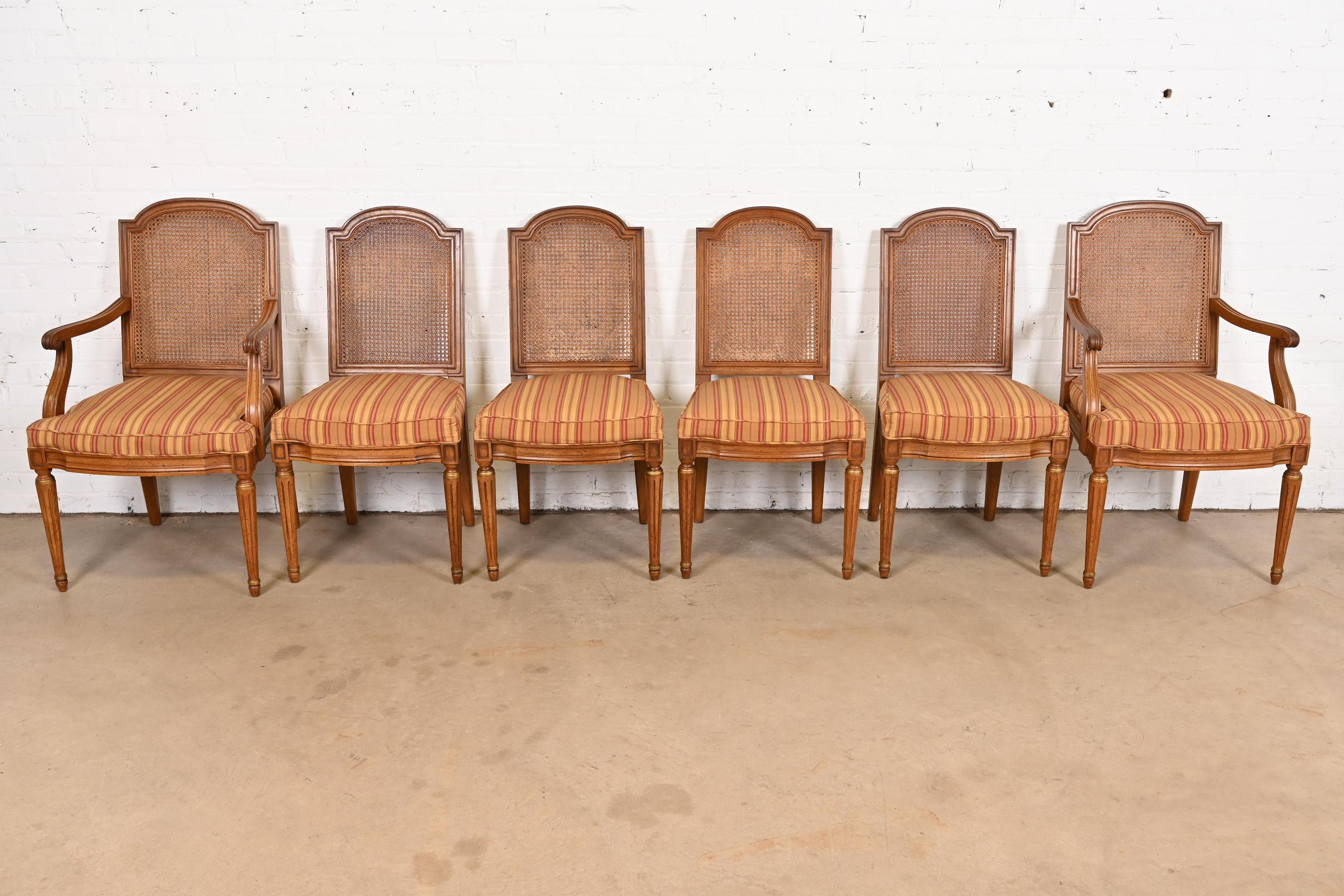 A gorgeous set of six French Regency Louis XVI style dining chairs

By Henredon

USA, Circa 1960s

Sculpted walnut frames, with gold gilt details, caned seat backs, and upholstered seats.

Measures: 
Side Chairs: 19