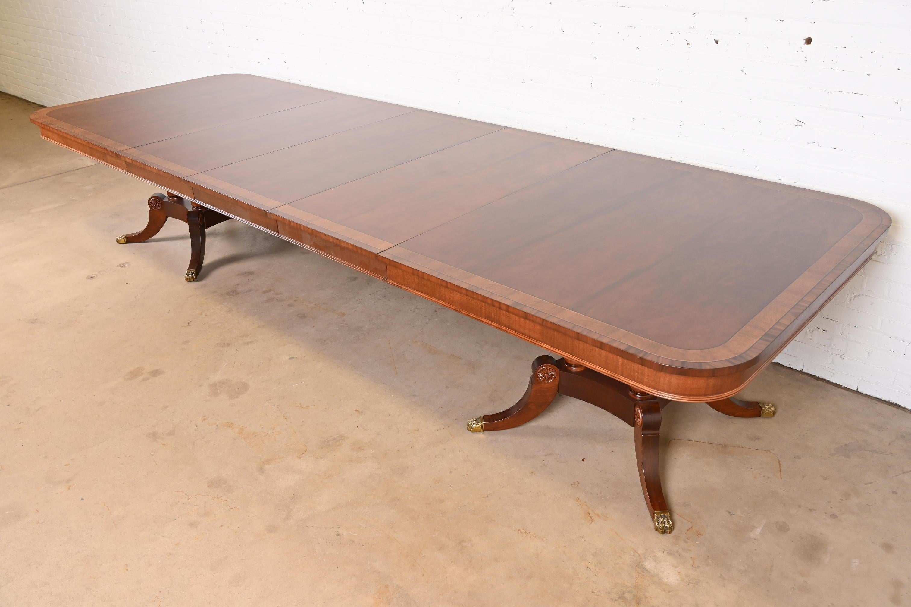 An exceptional Georgian or Regency style monumental double pedestal extension dining table

By Henredon

USA, Late 20th Century

Gorgeous book-matched flame mahogany top, with satinwood banding, carved solid mahogany pedestals, and brass-capped paw