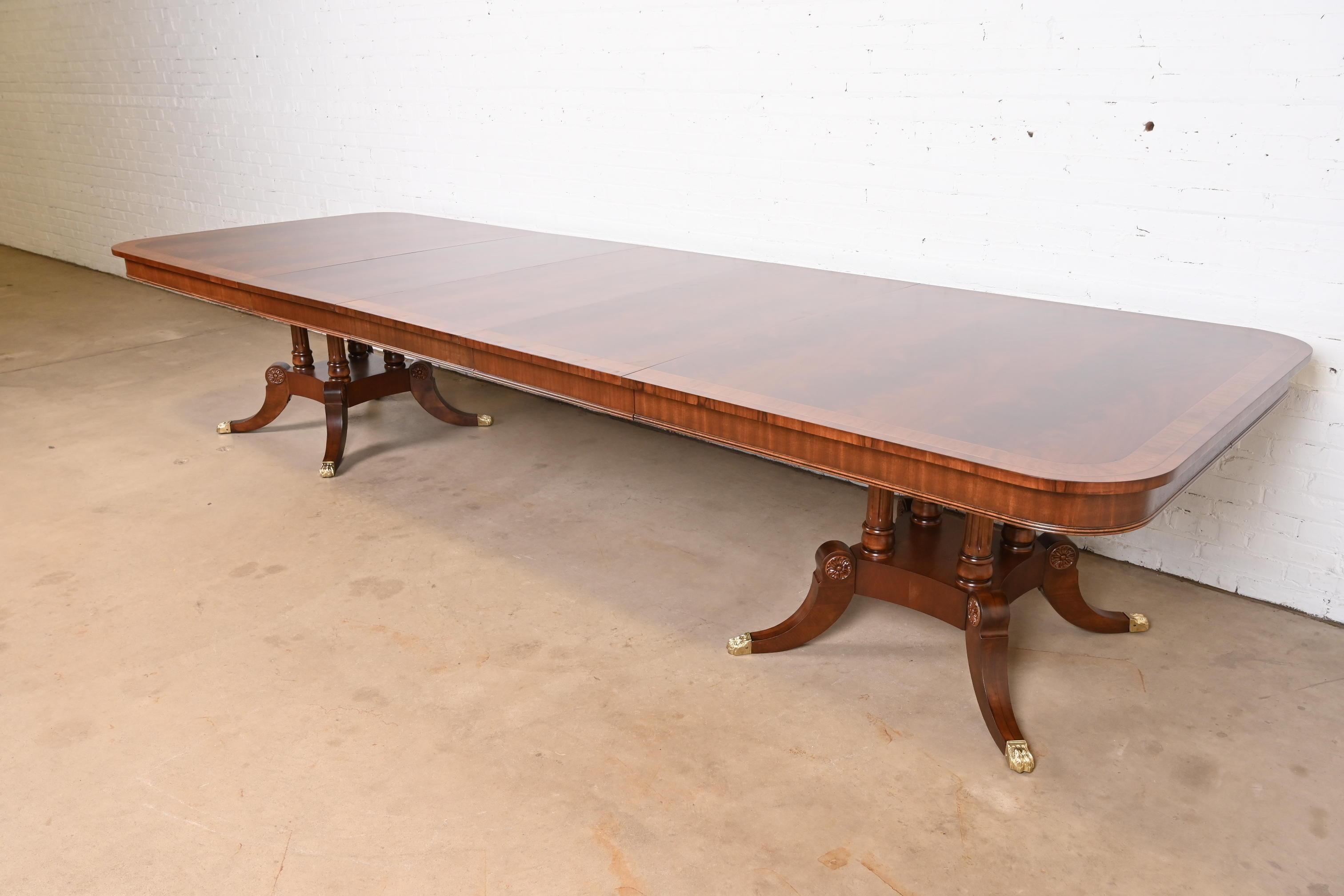 An exceptional Georgian or Regency style monumental double pedestal extension dining table

By Henredon

USA, Late 20th Century

Gorgeous book-matched flame mahogany top, with satinwood banding, carved solid mahogany pedestals, and brass-capped paw