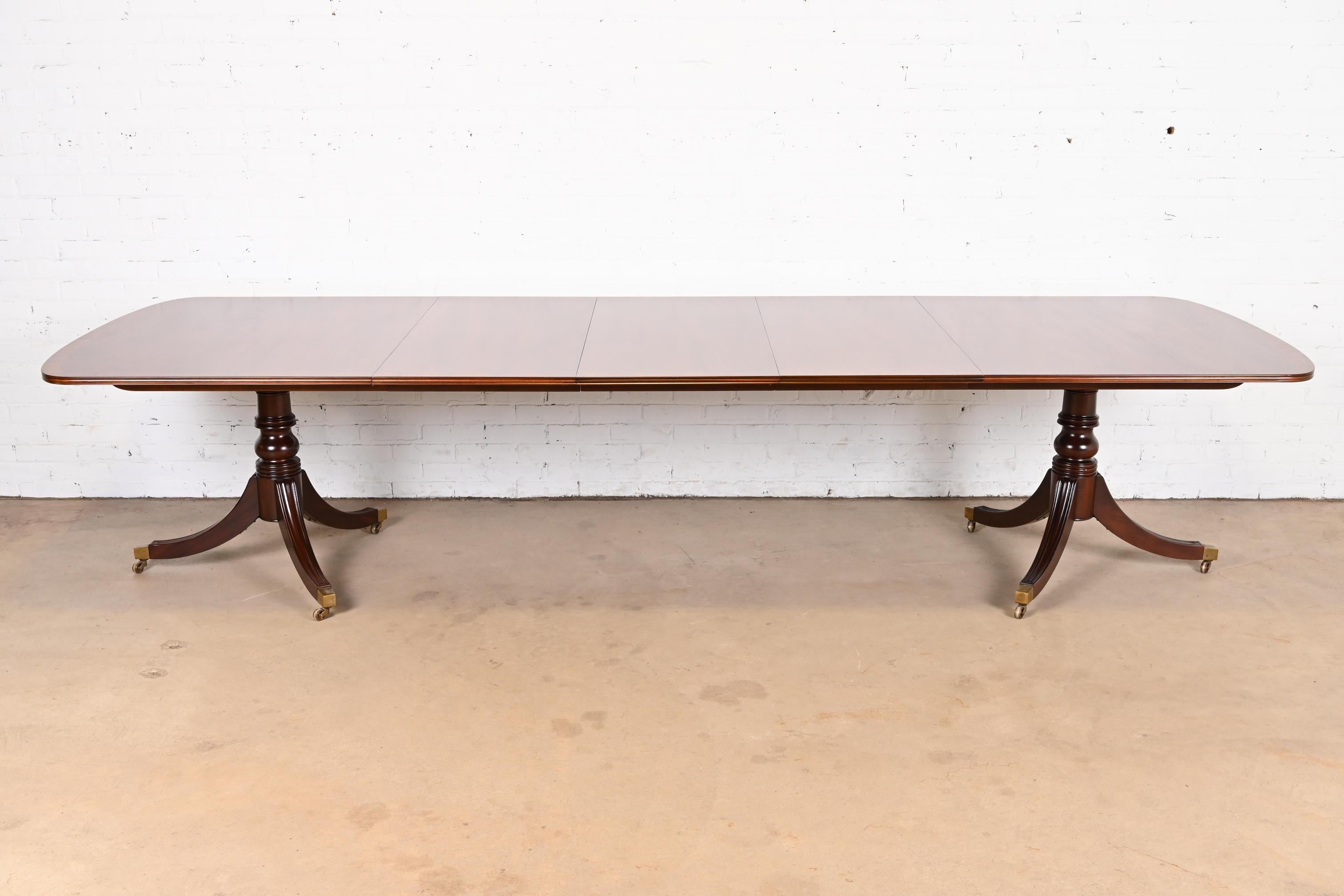 An exceptional Georgian or Regency style double pedestal extension dining table

By Henredon

USA, Circa 1980s

Gorgeous banded mahogany, with ebony string inlay, carved solid mahogany pedestals, brass-capped feet, and brass casters.

Measures: 72