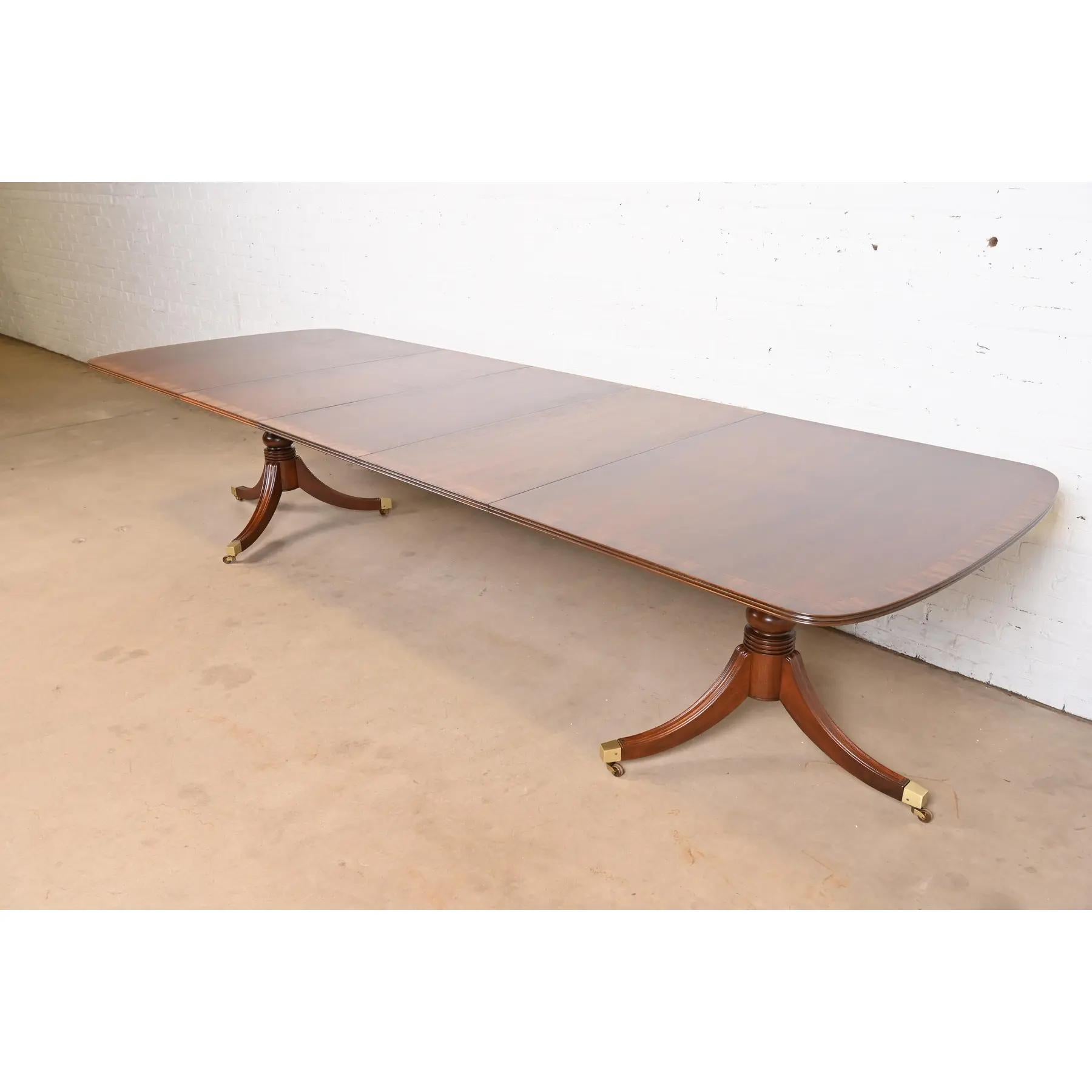 Exceptionnelle table à manger à rallonge à double piédestal de style Géorgien ou Régence.

Par Henredon

USA, Circa 1980

Magnifique acajou, avec bandes de bois satiné, piédestaux en acajou massif sculpté, et pieds coiffés de laiton sur roulettes en