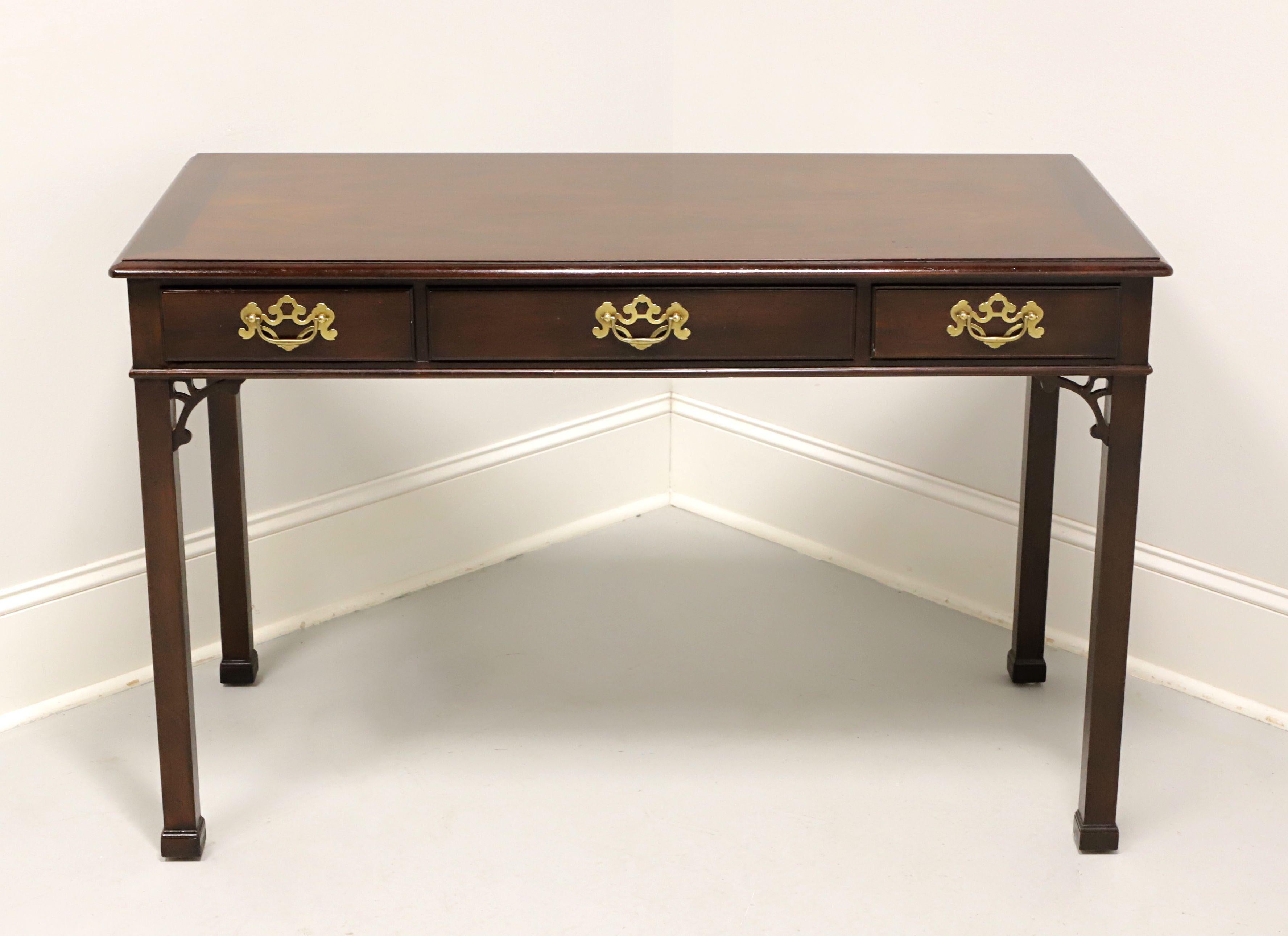 A Chippendale style writing desk by Henredon. Mahogany with banded bevel edged top, brass hardware, decorative fretwork arches to corners, square straight legs, and cap feet. Features three drawers of dovetail construction, with center drawer having