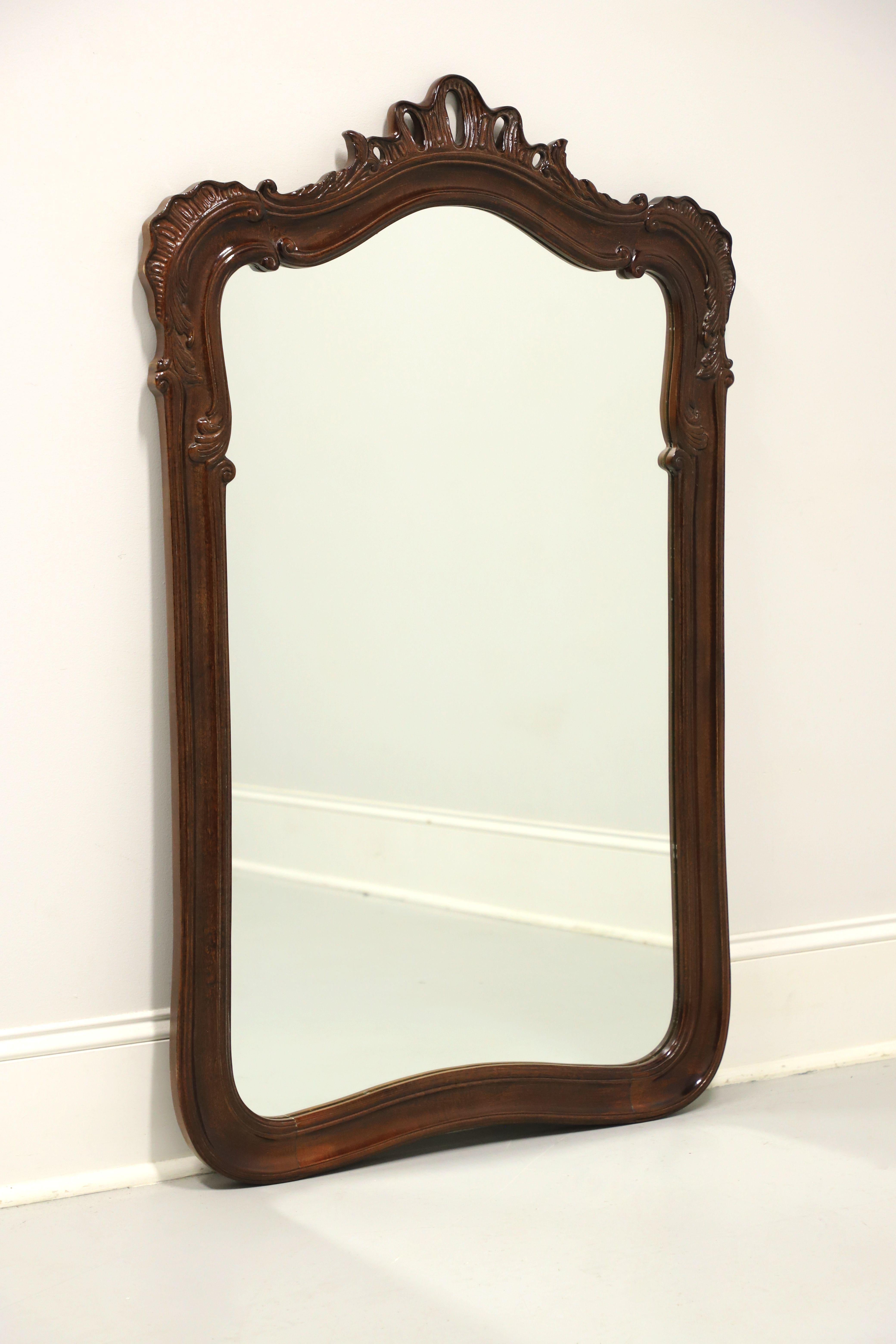 A French Country Louis XV style wall mirror by Henredon. Mirrored glass in a mahogany frame. Frame features an arched and decoratively carved top with an open crown-like carving to the center. Made in Morganton, North Carolina, USA, in the late 20th