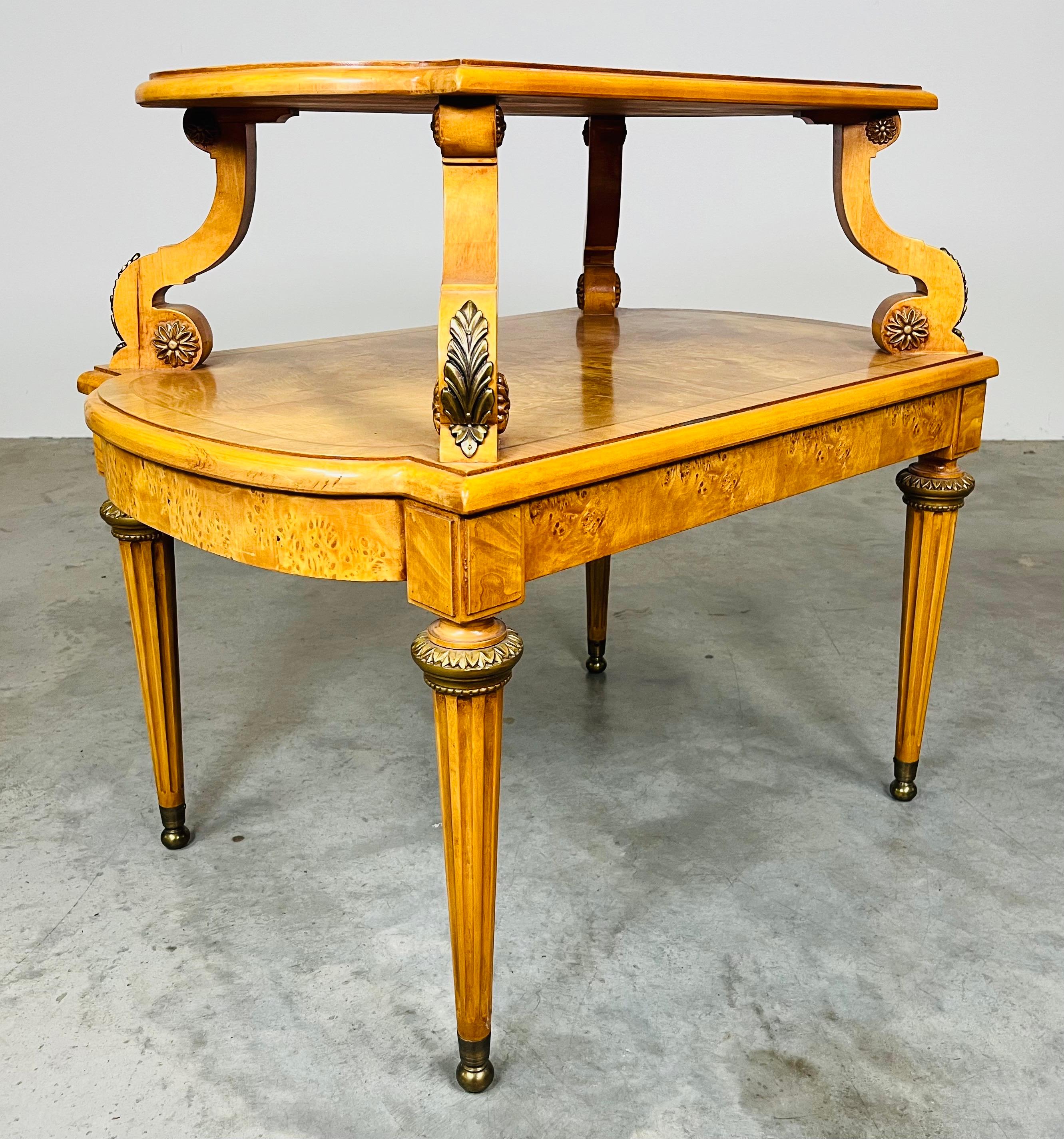 A beautiful French Empire style olive ashwood burled end table by Henredon. Exceptionally designed having 2 tiers with gold gilt scrolled supports. Features brass mounts and ball feet under fluted tapering legs. The perfect compliment to any