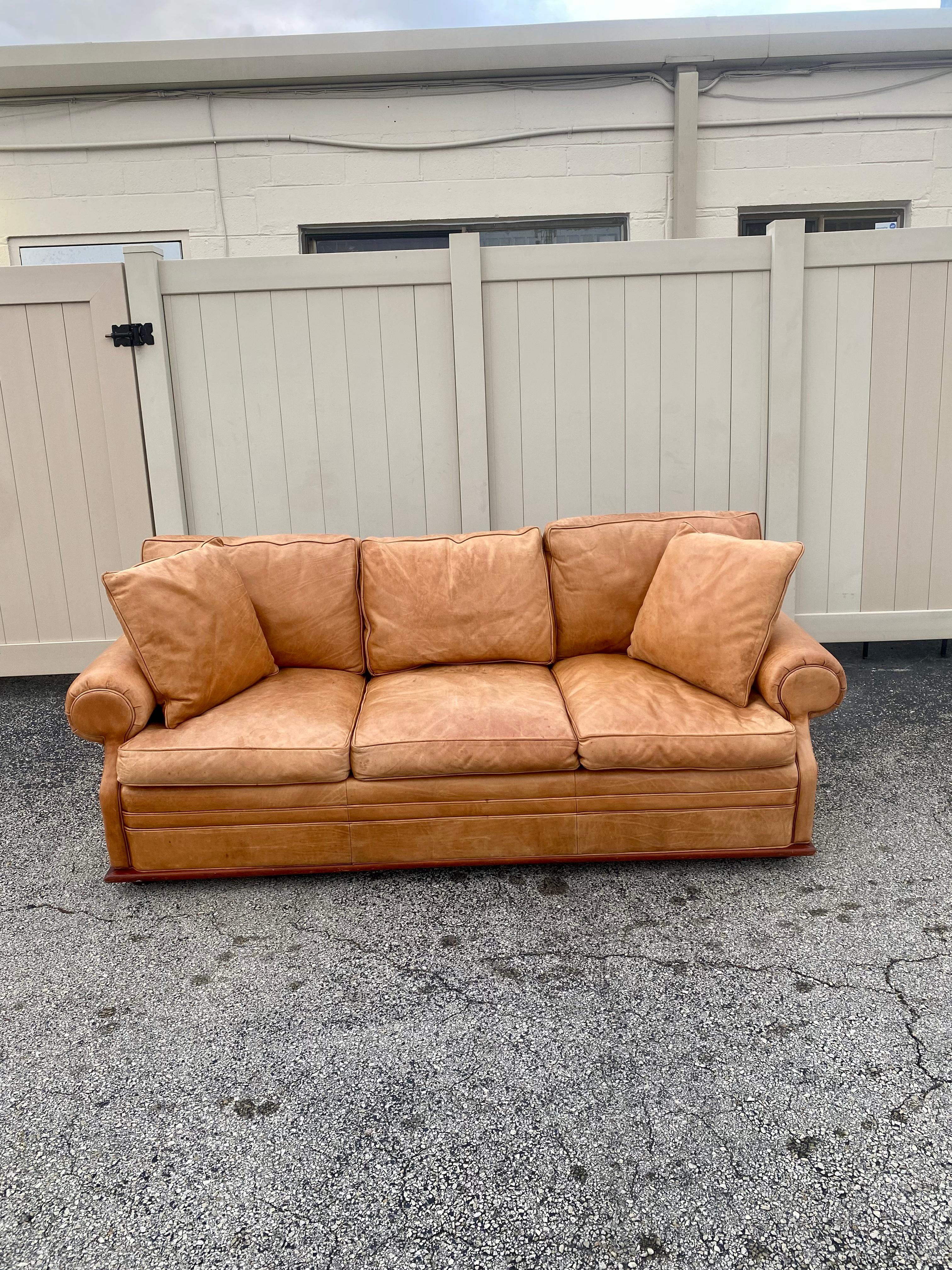Stunning Ralph Lauren sofa in thick, buttery, luxurious saddle leather. Lovely light patina. Sink in comfort with the softest down filled cushions. Low profile angular dark wood plinth base wraps around entire sofa, creating a floating appearance,