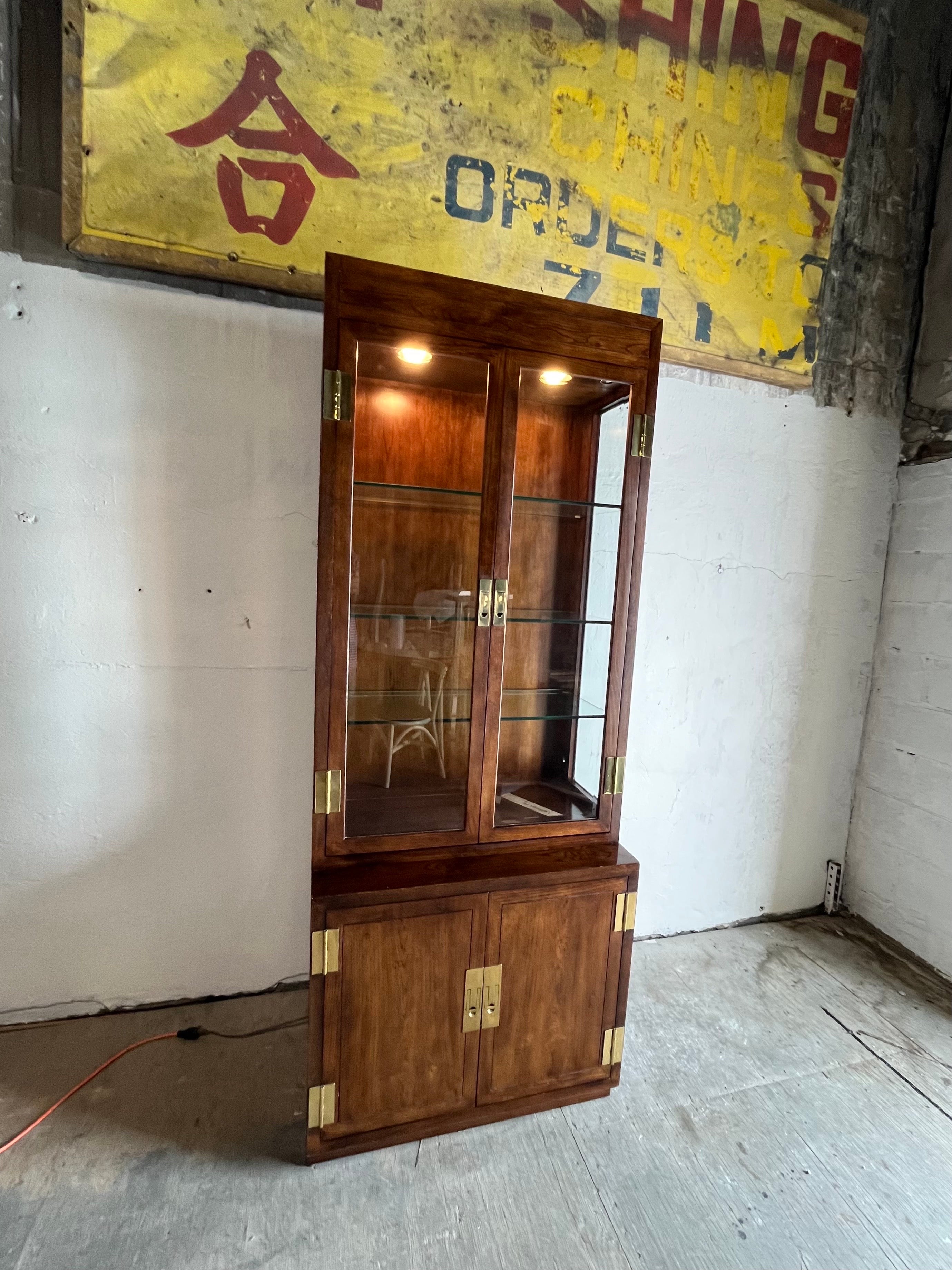 Design senza tempo in questa vetrina Campaigner di Henredon Scene One. Linee classiche e snelle con ferramenta in ottone incastonata. Mobile inferiore a 2 ante con ripiano regolabile, 3 ripiani in vetro regolabili nel mobile superiore con interno