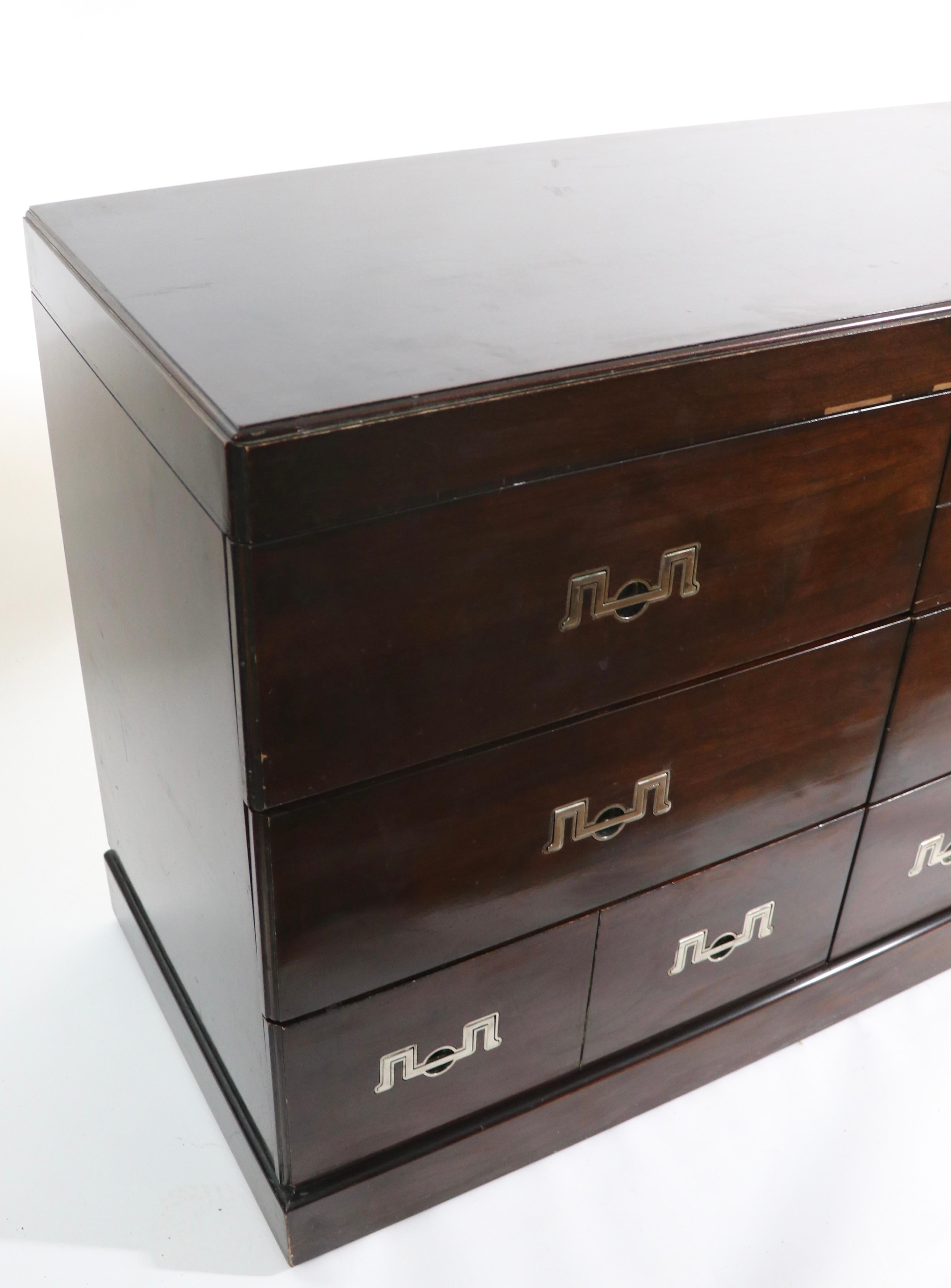 Massive and impressive Henredon triple dresser, having three banks of three drawers, each with a stylized chrome bale form handle. The dresser is even in color ( dark ), the lighting in the images is uneven. The case is of dark mahogany in gloss
