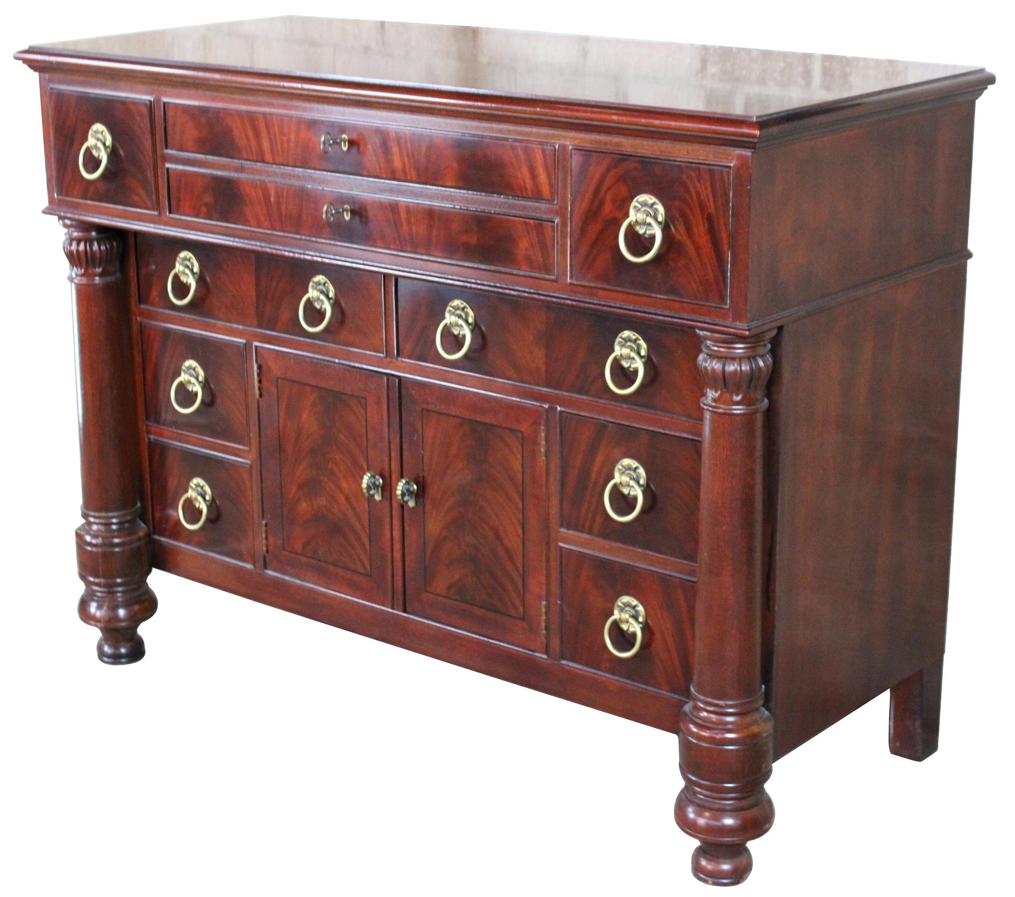 An exceptional example of French Empire styling by Henredon Industries. Made from crotch mahogany with ten drawers and lower cabinet for storage. Includes beautifully turned and carved columns, a beveled hanging mirror, brass knocker pulls and two