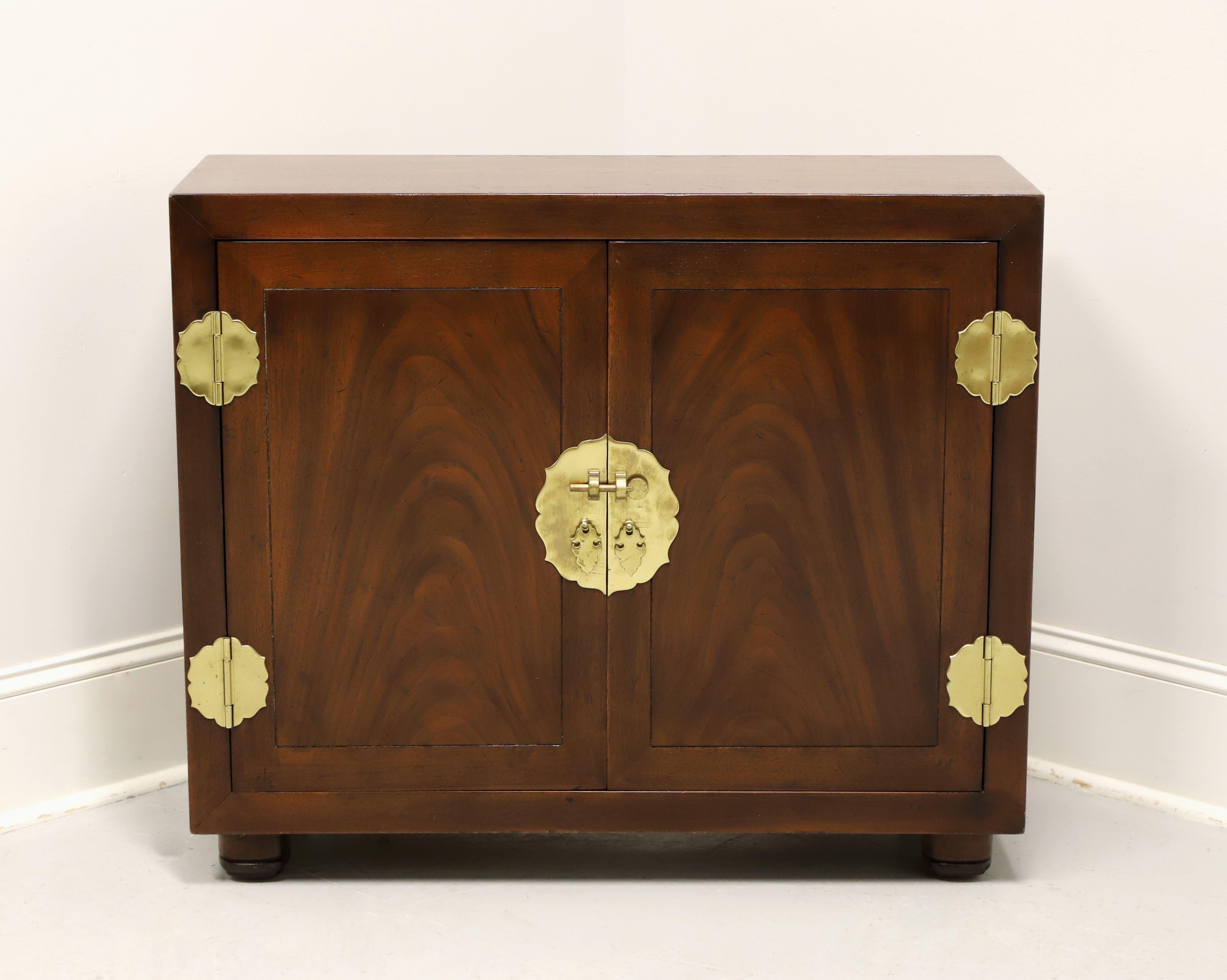 A console cabinet in the Japanese Tansu Campaign style by Henredon. Mahogany with smooth surface top, brass hardware & accents, inset flame mahogany to doors, and bun feet. Features two doors revealing interior storage with one adjustable wood