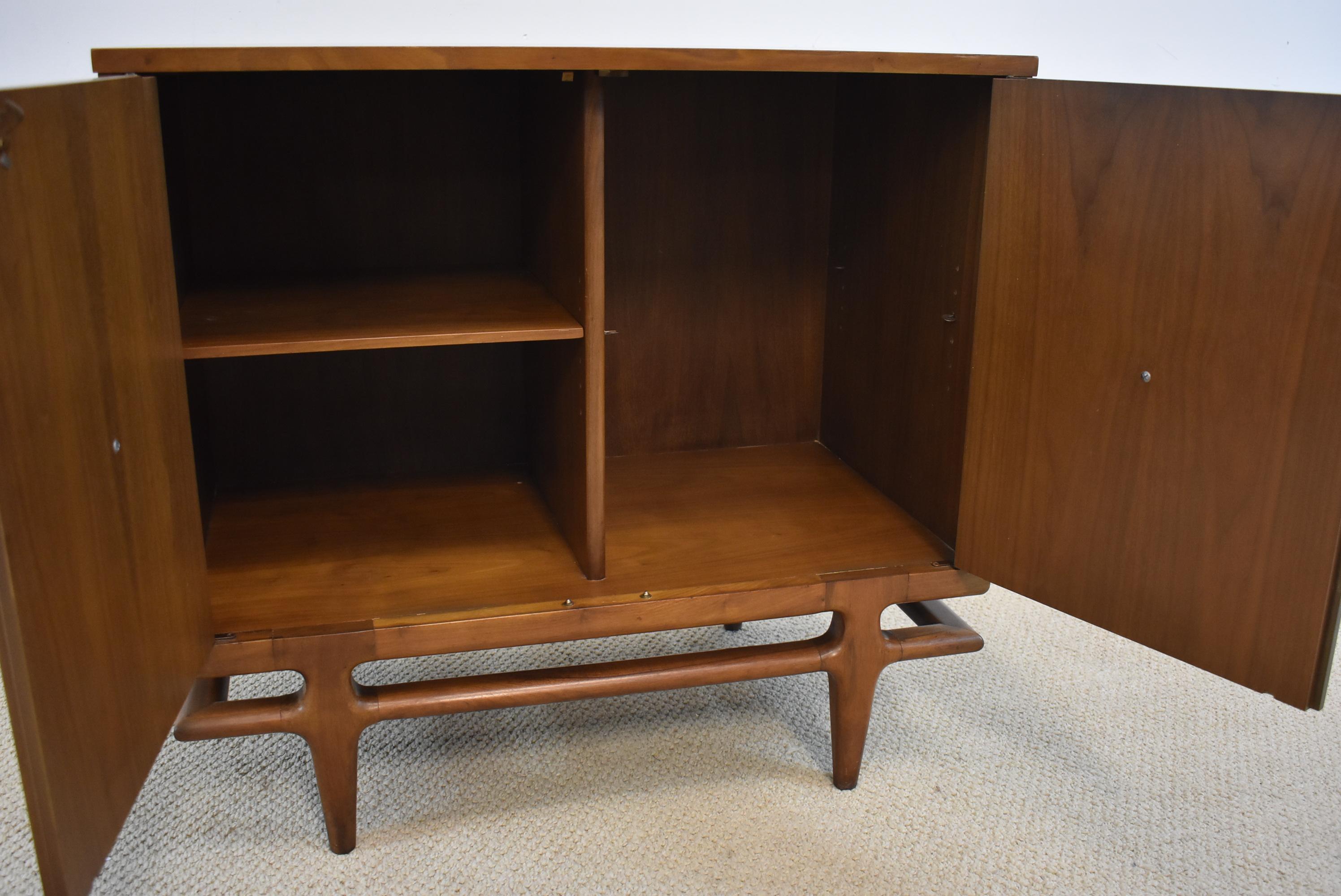 Mid-Century Modern by Henredon Furniture in walnut with two doors. Single adjustable interior shelf. Unusual door pulls that may be Bakelite. Great piece for a record cabinet or liquor cabinet. 