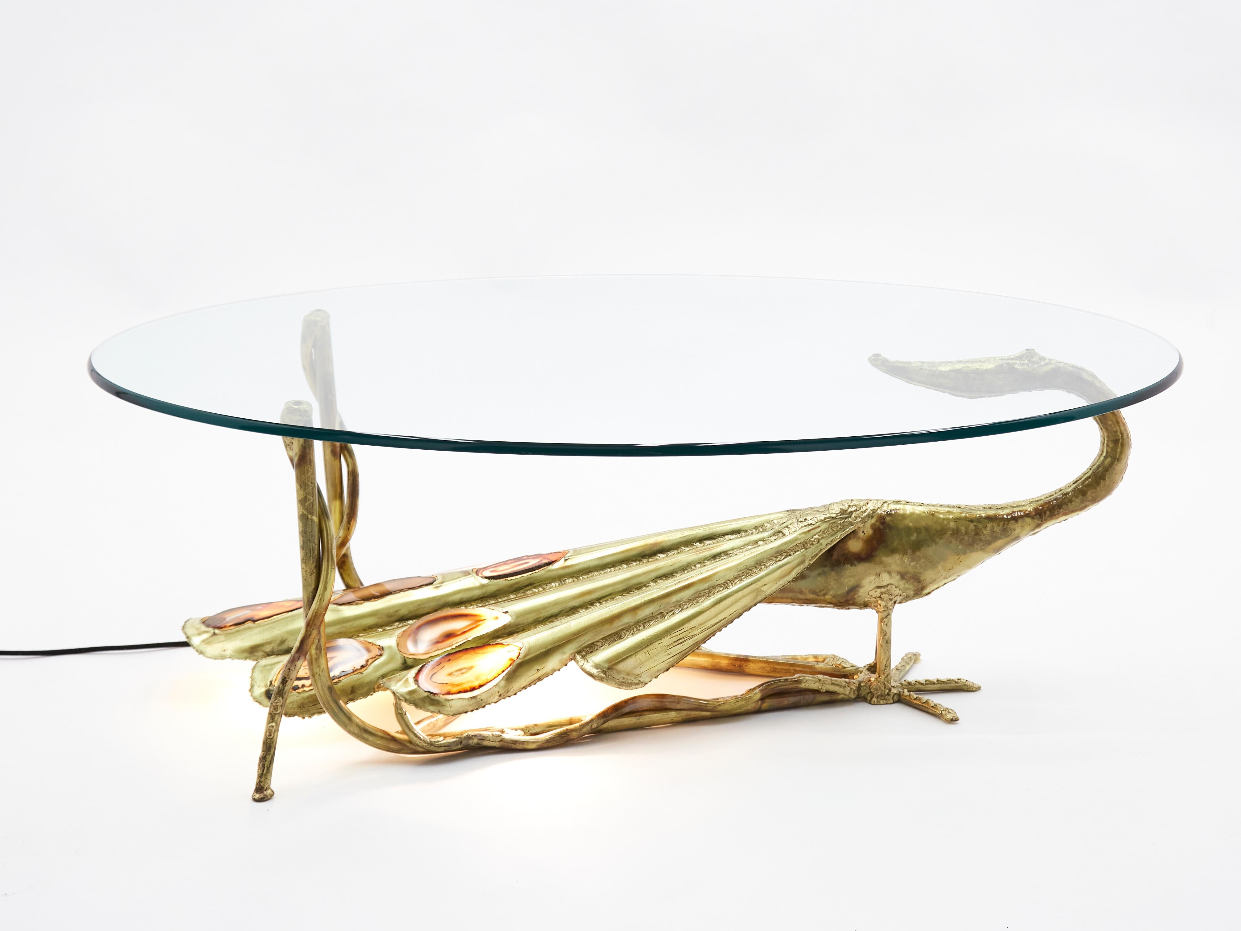 This unique signed Henri Fernandez 1970s coffee table radiates eclectic flair. Produced for Maison Honoré Paris in the late 1970s, it features a bevelled glass top that reveals a beautiful bronze peacock sculpture with mesmerising agate stones. The