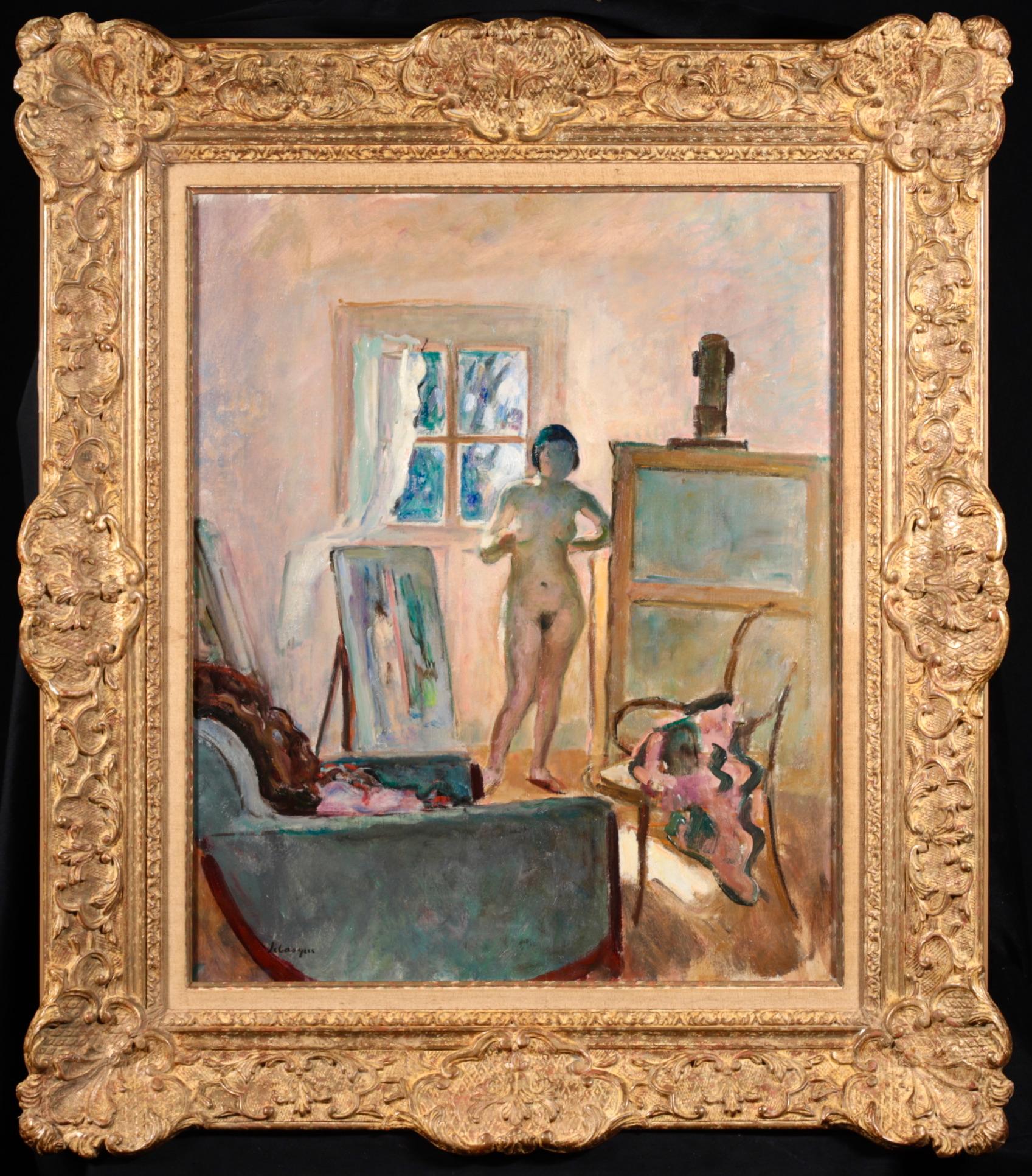 Signed oil on canvas nude in interior circa 1910 by French post impressionist painter Henri Lebasque. The work depicts the woman posing in the artist's studio. There are clothes draped over a chair and velvet armchair in the foreground. The model