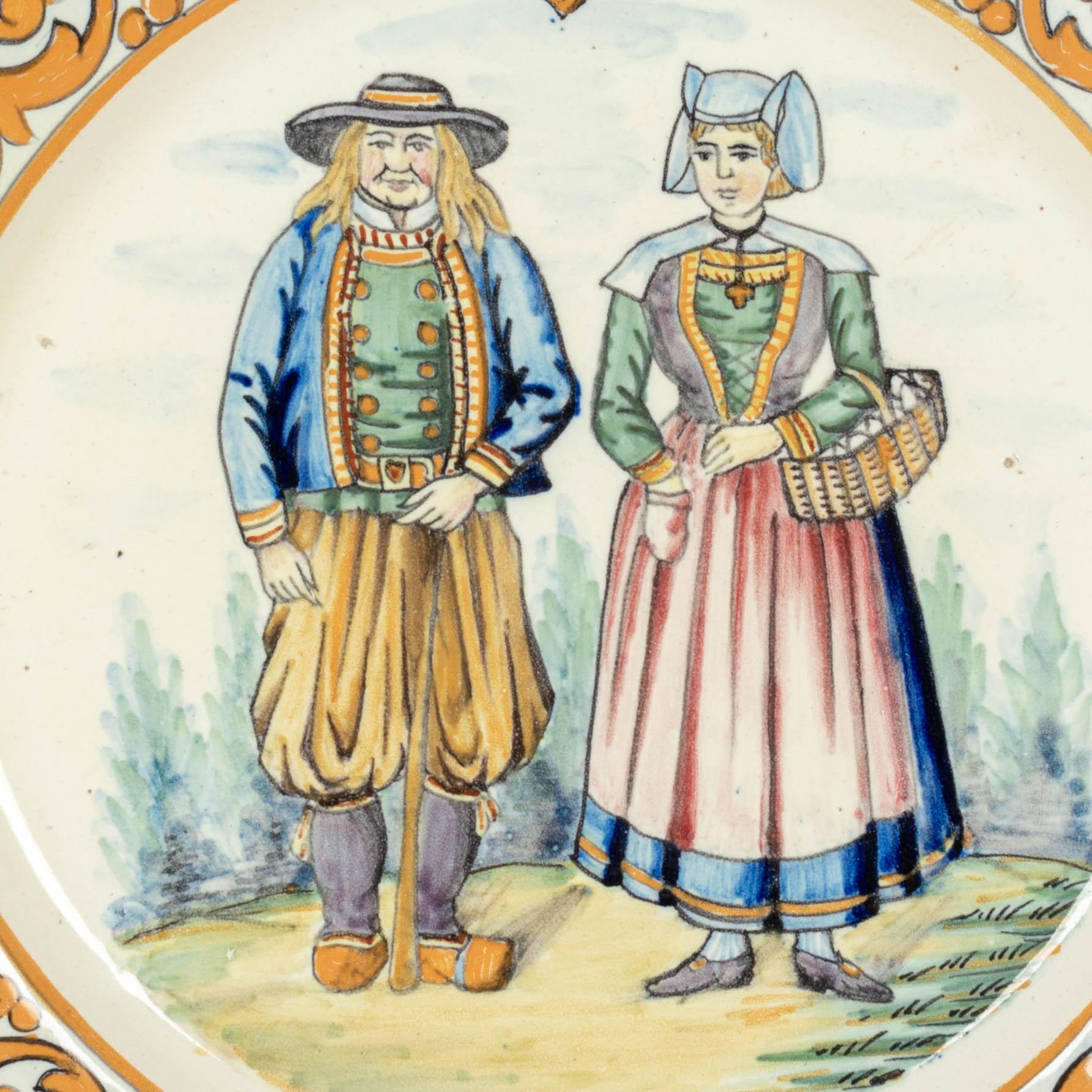 Handbemalter dekorativer Teller aus französischer Fayence von Henriot Quimper, der ein bretonisches Paar in traditioneller Kleidung zeigt. Orangefarbene Umrandung mit Blättern und einem Wappen der Quimper-Krone oben. Ein dicker Teller von guter