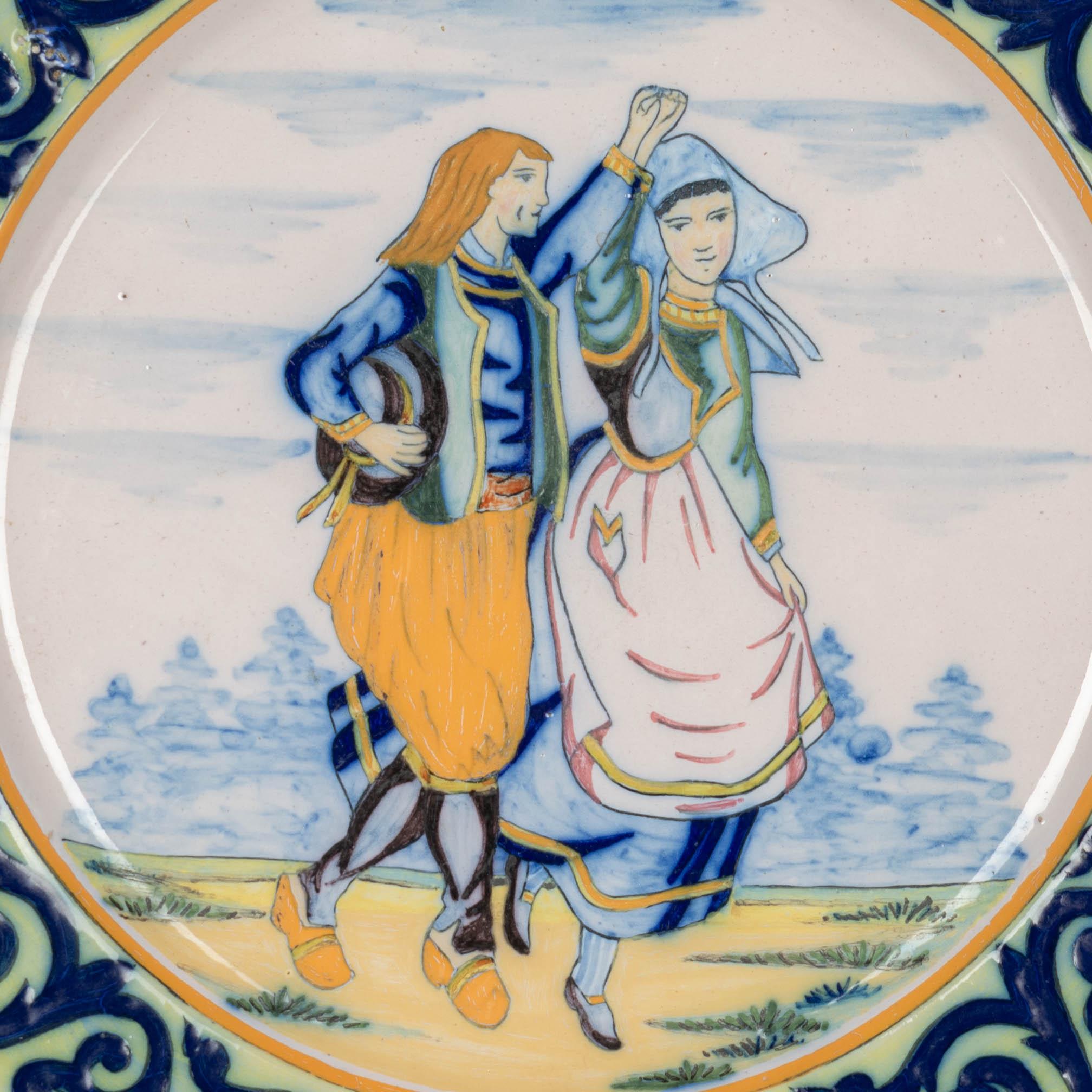 A Henriot Quimper French faience hand painted decorative plate, depicting a Breton couple dancing. Blue foliate border with Quimper crest at the top. A good quality, thick plate with minor loss to glaze. Mark on back: HR Quimper.