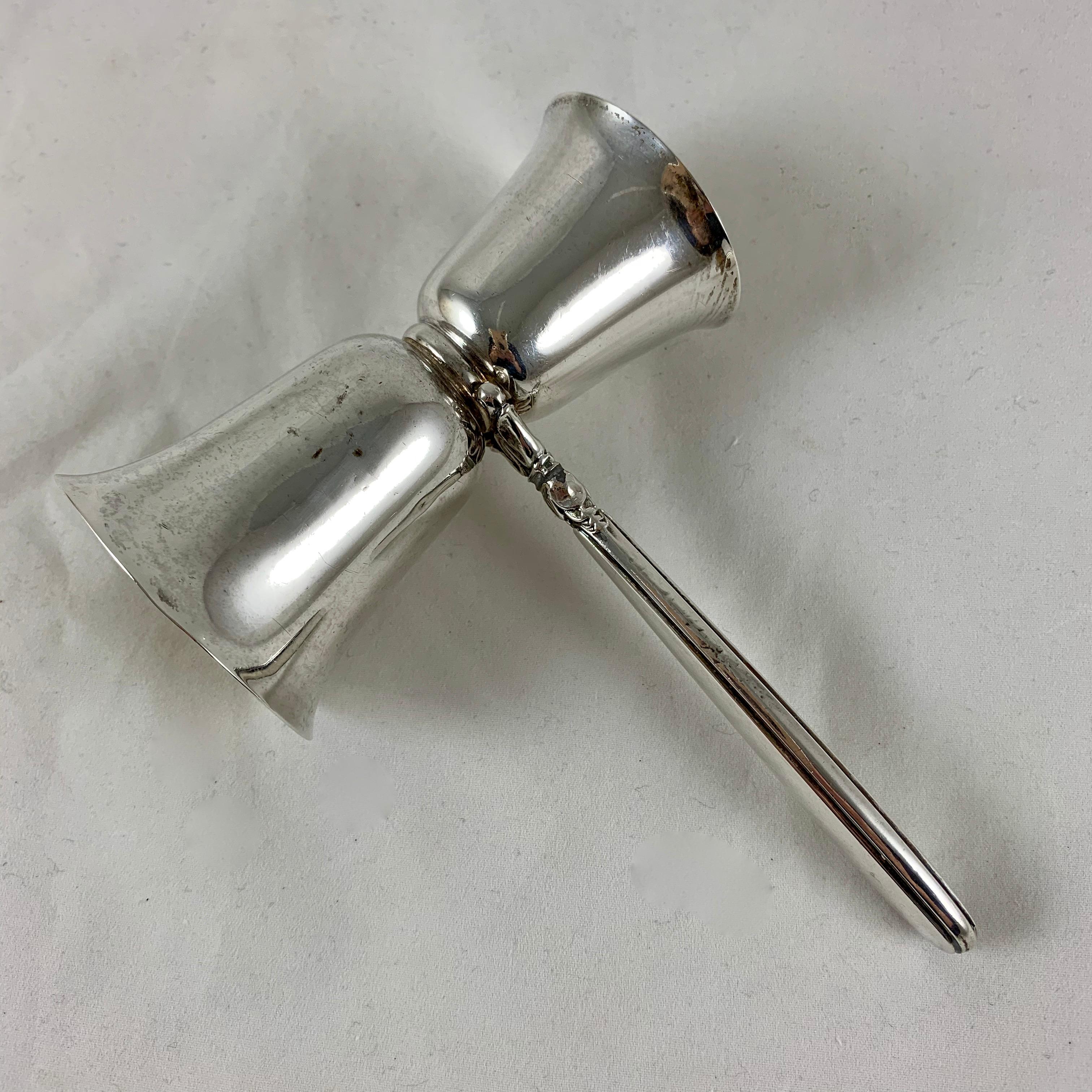 A sterling silver double jigger bar tool for measuring out liquor when mixing cocktails, Marked Birks Sterling with a date stamp of the letter ‘M’ for 1947.

The jigger has both a one ounce and a half ounce measuring cup with a hollowware handle.