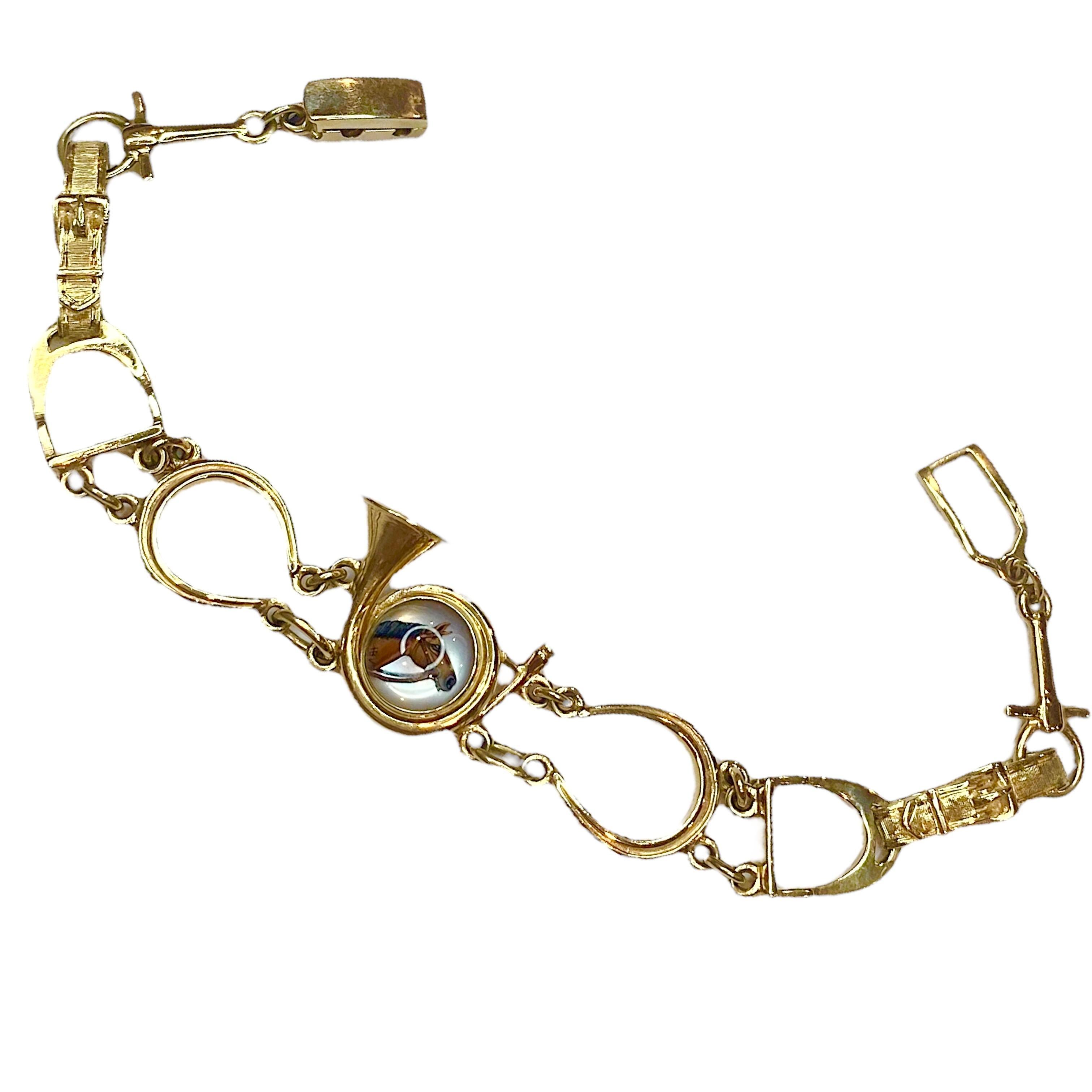 Bracciale in oro giallo 14K di Henry Blank & Co. con un cabochon di cristallo Essex con una testa di cavallo smaltata rivolta verso destra, incastonato in una maglia a forma di corno e sostenuto da scarpe e staffe di cavallo. Finitura lucida e