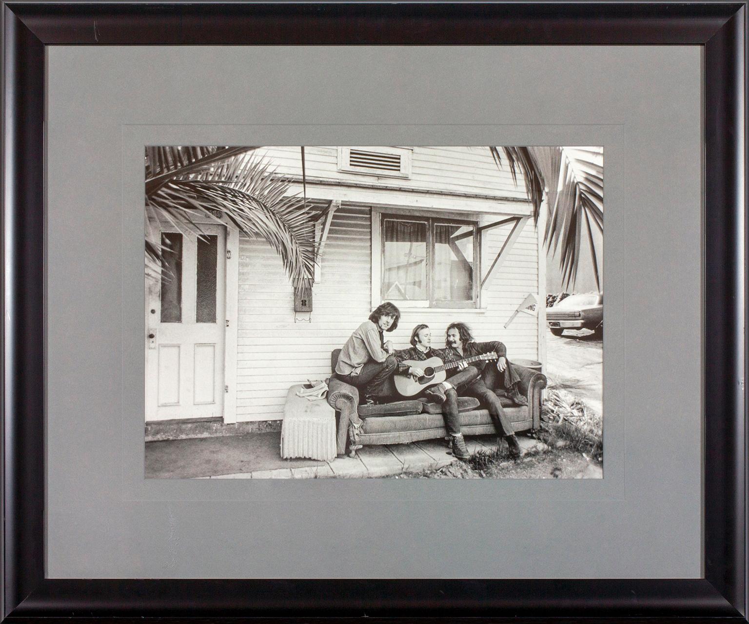 Outtake photo from 1969 Crosby, Stills & Nash album cover photo session in West Hollywood, California, by photographer Henry Diltz. Depicts David Crosby, Stephen Stills and Graham Nash sitting on a couch outside a house. This framed photo was