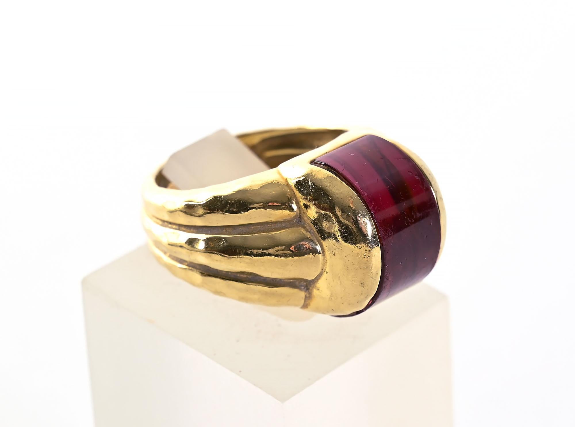 Sporty tourmaline ring set in 18 karat gold by American designer, Henry Dunay. The half round cabochon stone is set in Dunay's often used hammered gold with triple banding throughout the ring.
In addition to Dunay's signature is the style number