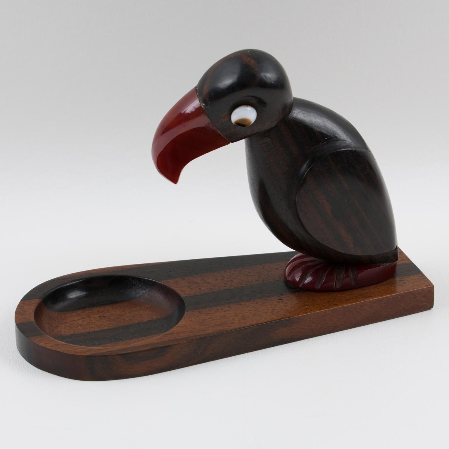 Stylish English Art Deco Henry Howell & Co Ltd, YZ bird novelty ashtray or catchall, dating from the 1920s-1930s for Alfred Dunhill Ltd.
This funny standing bird has a carved Macassar wood body with a cherry red amber Bakelite beak, feet and glass
