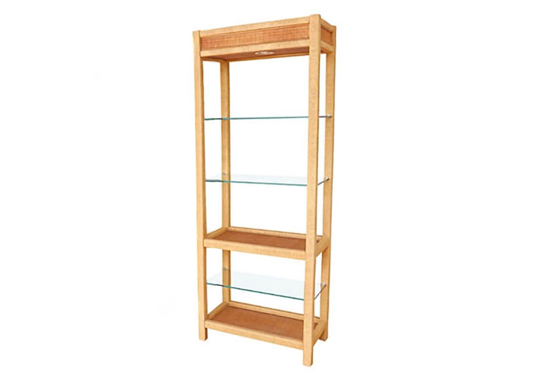 A rattan and glass etagere designed by Henry Link for Lexington Furniture Co. Three glass shelves rest in a rattan wrapped open frame supported with a central lower rattan shelf. Lit with a single light on top.
 