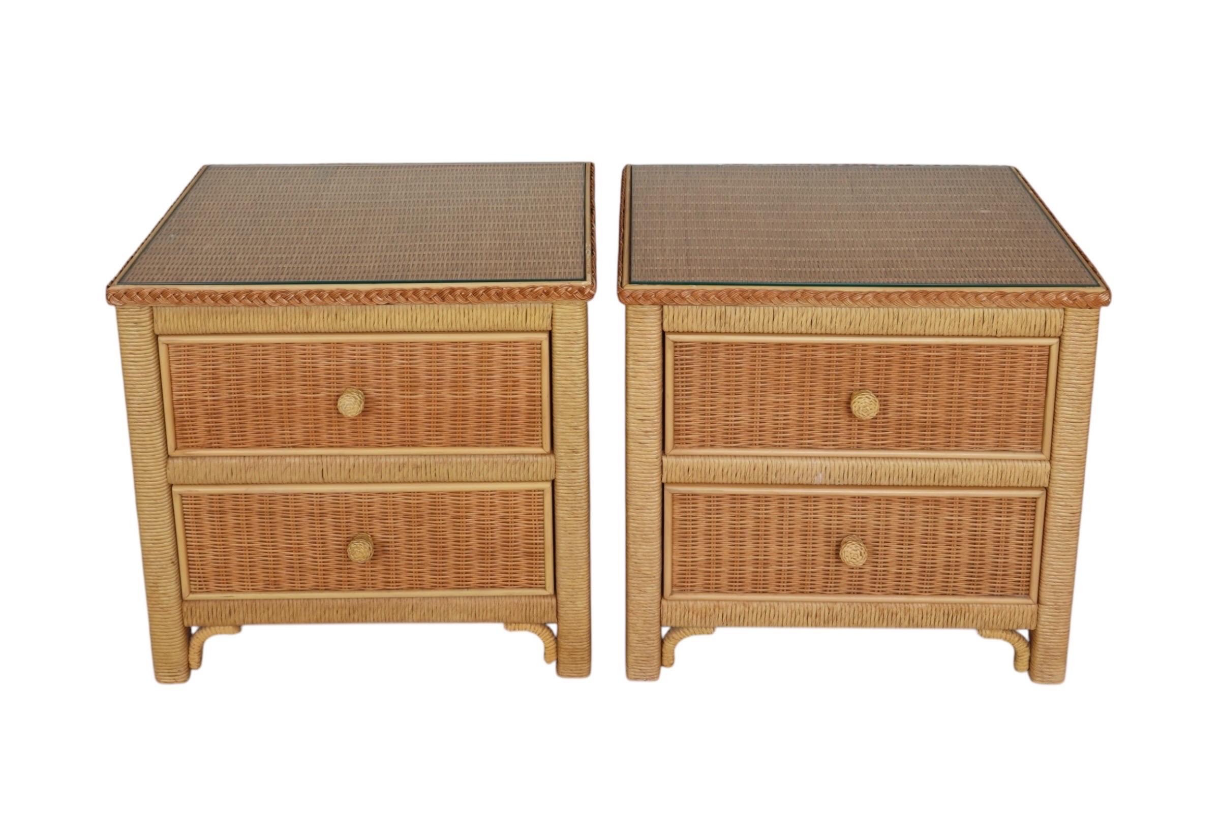 A pair of Henry Link nightstands made of wicker. Decorative braided bands surround protective glass tabletops, and below two wooden draws open easily with round woven mushroom knob handles. Marked Henry Link inside the top drawer. Dimensions per