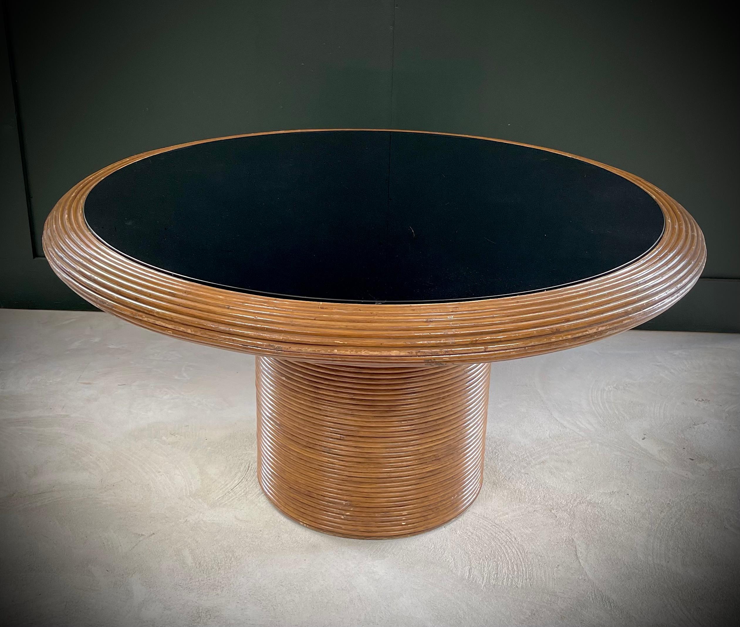 Transform your dining space into a timeless retreat with this exquisite Henry Olko Round Pencil Reed Dining Table. Crafted in the 1970s for Willow and Reed, it exudes elegance with its split reed pedestal base and sleek black glass top. Perfect for
