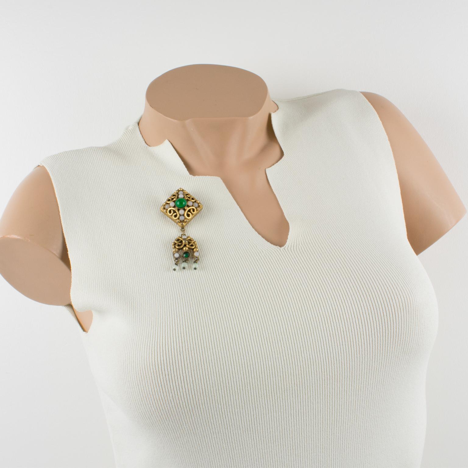 Elegante broche de bronce dorado del diseñador de joyas francés Henry Perichon (también conocido como Henry). La forma colgante con influencias del diseño medieval se adorna con cabujones de vidrio vertido en colores surtidos verde esmeralda y
