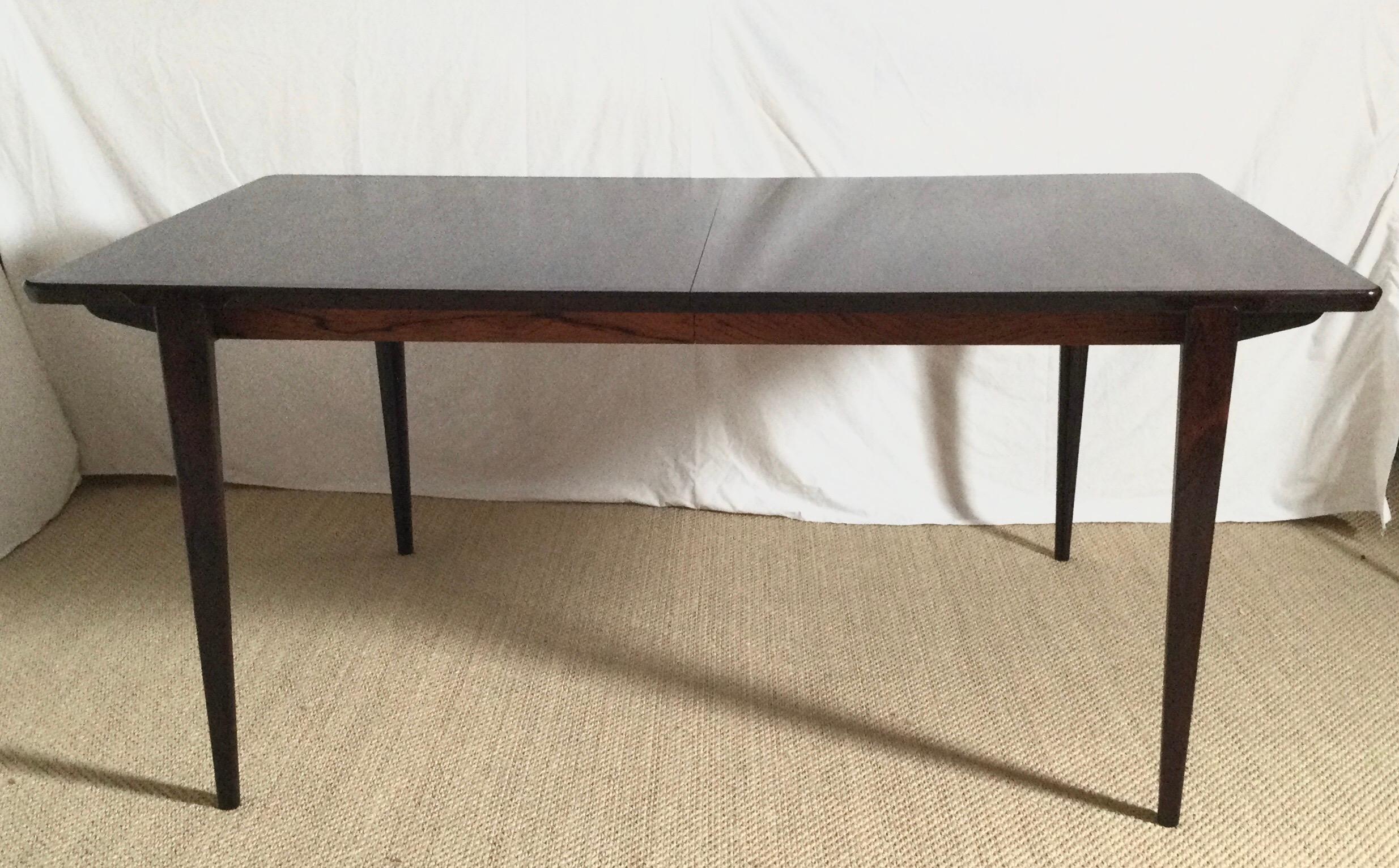 Elegant rosewood dining table by Henry Rosengren Hansen produced by Brande Mobelfabrik. A solid edge top floats above a sculpted rosewood base with legs. The table 65 inches long with two 17 inch leaves that are stored inside the table. Fully opens