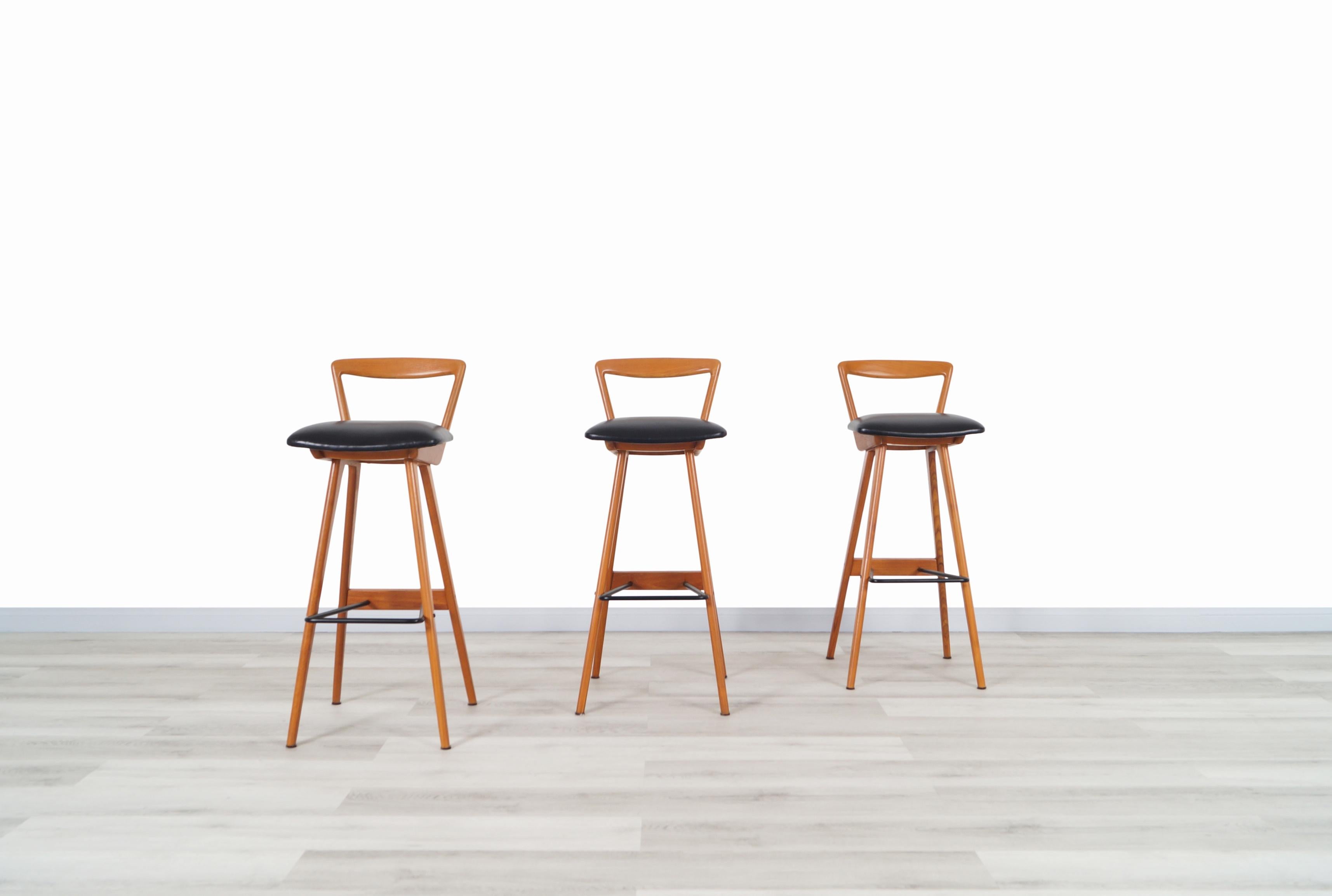 A very rare set of three Danish teak bar stools designed by Henry Rosengren Hansen and produced by Brande Møbelindustri in Denmark. These exceptional bar stools feature a sleek and sculptural boomerang shaped frame with solid teak wood construction,