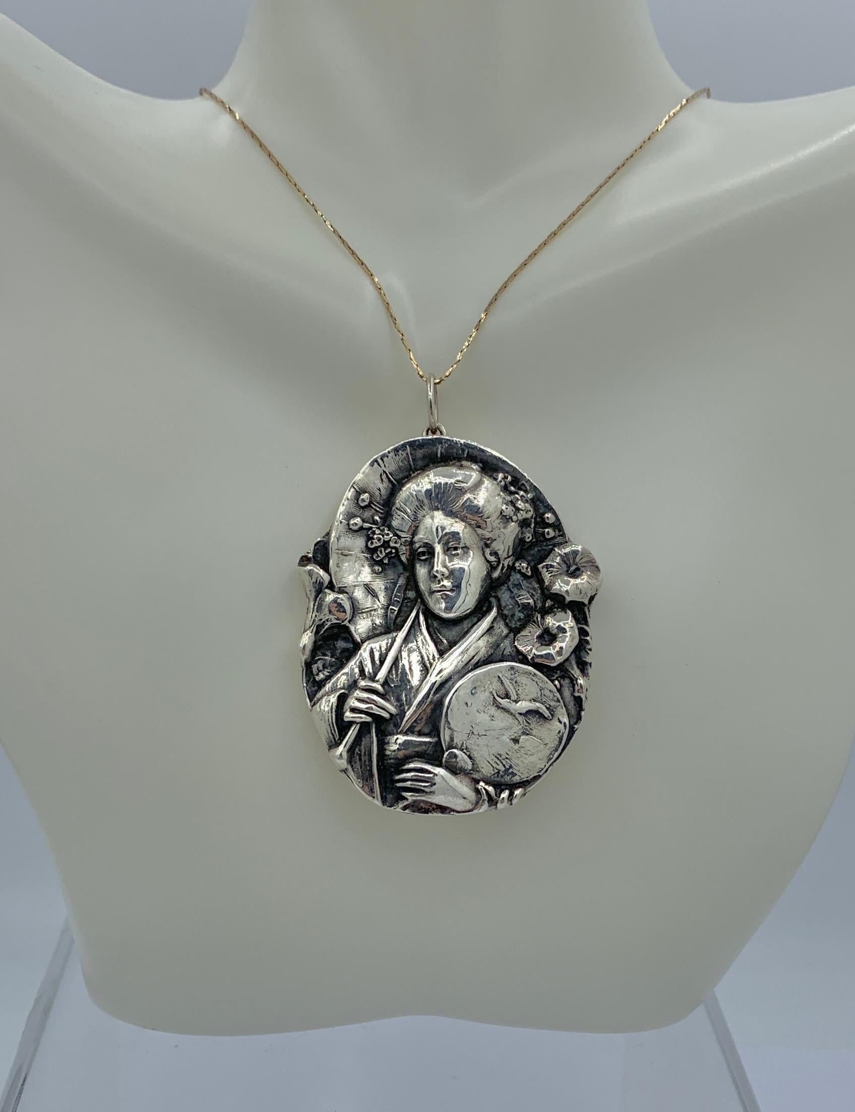 This is a stunning Sterling Silver pendant by Henryk Winograd featuring a gorgeous deep repousse image of a Japanese Geisha with her fan adorned with a flying crane, flowers and stunning hair adornments.  The pendant is in the gorgeous nature
