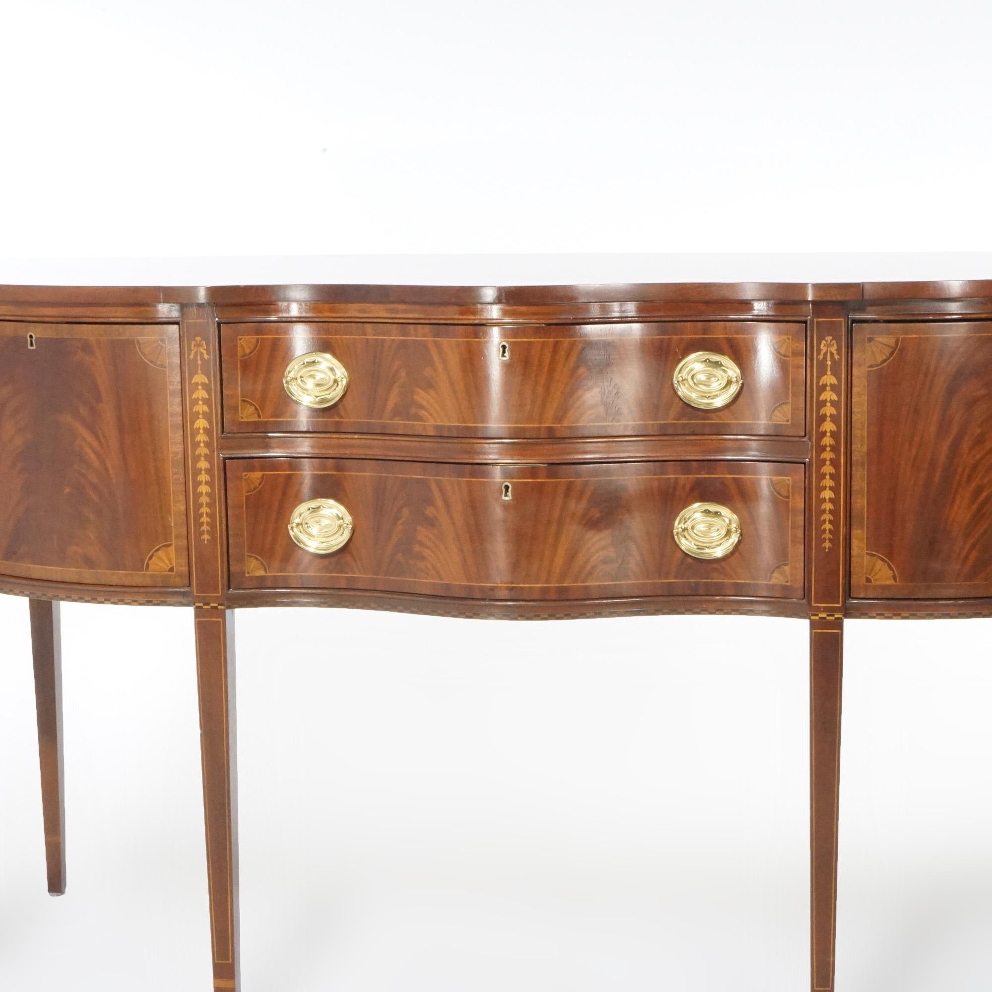 An English Hepplewhite style sideboard by Council Craftsmen offers flame mahogany construction in serpentine form with two drawers having flanking cabinets, inlaid satinwood banding and stylized inverted bellflower garland, raised on straight taper