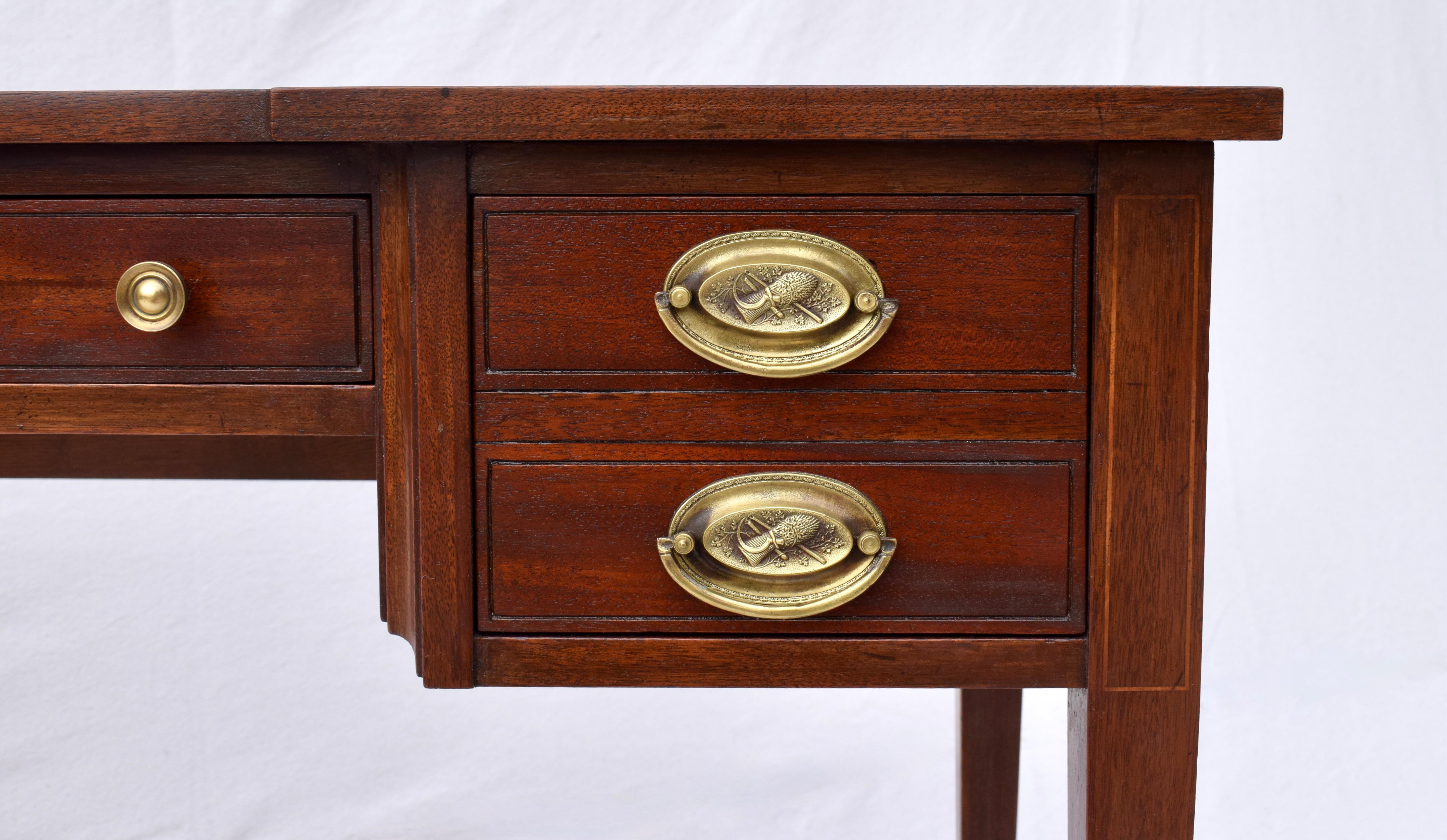 Charak Furniture Table à écrire à cinq tiroirs en acajou de style Hepplewhite anglais, avec de remarquables cuivres ovales, une serrure et une clé en état de marche, reposant sur des pieds fuselés et des roulettes. 