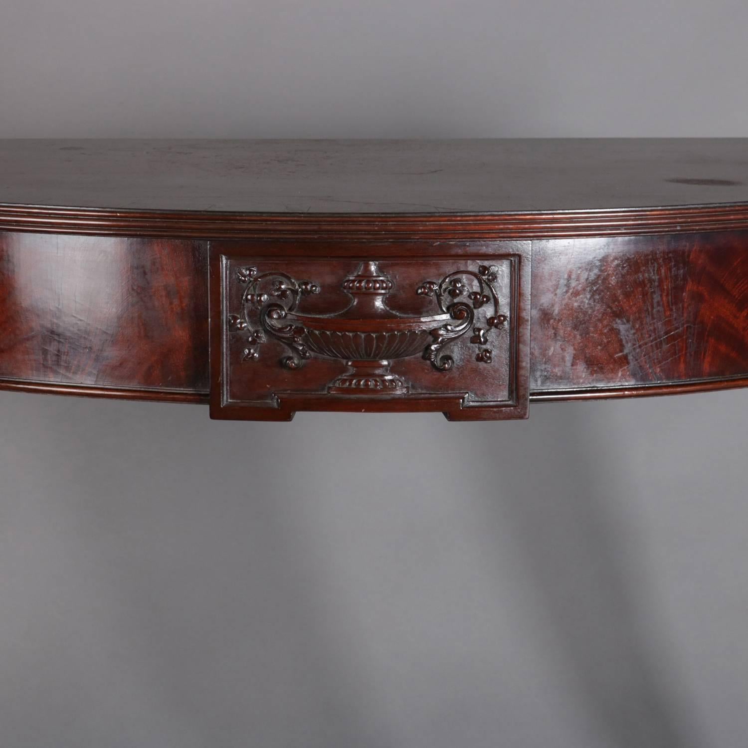 Hepplewhite style carved mahogany console table features demilune form with satinwood inlay banded top over apron having central caved urn and flanking rosette joints supported by reeded and tapered legs terminating in spade feet, 20th