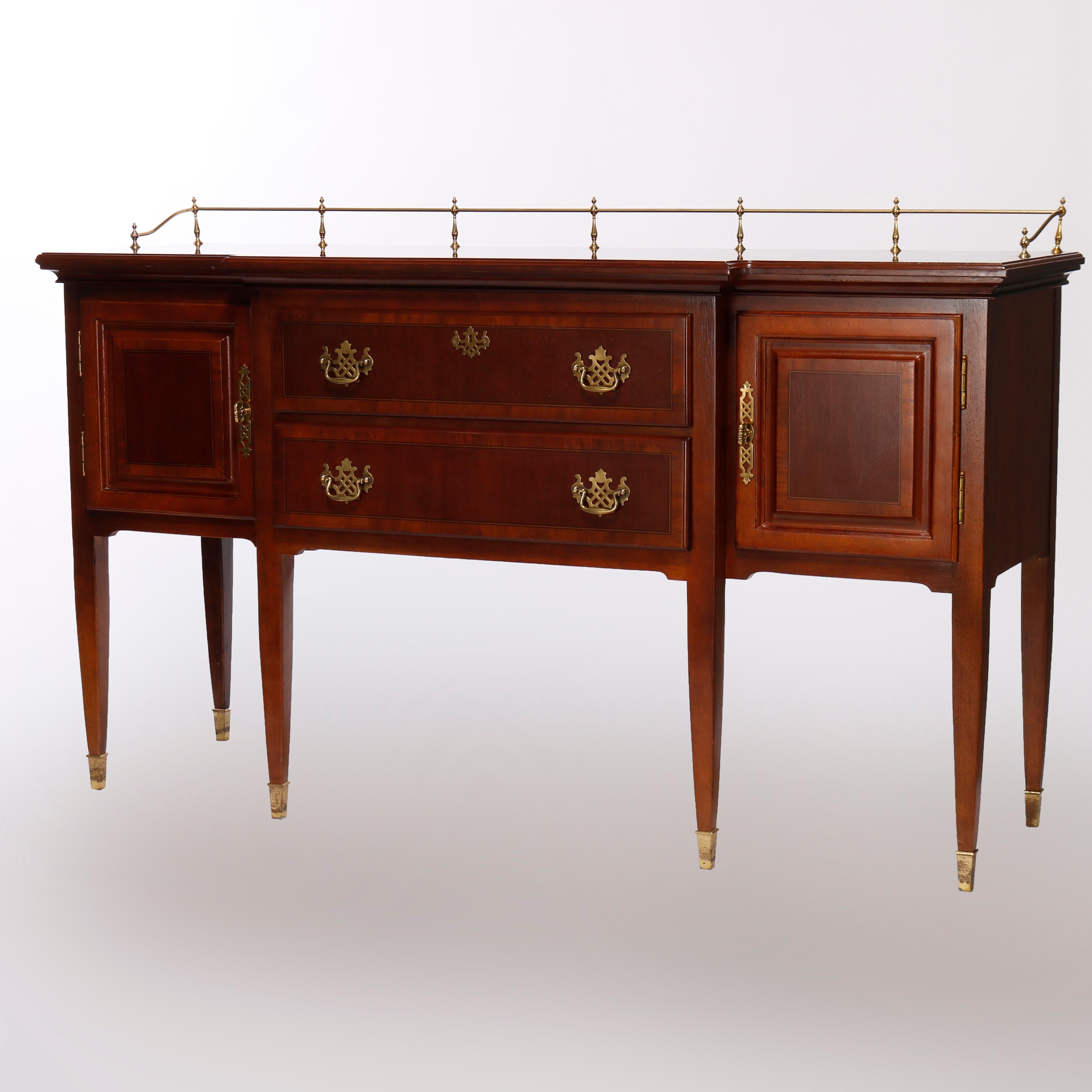 A Hepplewhite style sideboard offers mahogany construction with shaped top having brass rail over case with two crossbanded drawers with flanking cabinets having paneled doors, raised on tapered and straight legs, 20th century

Measures - 38.75''H