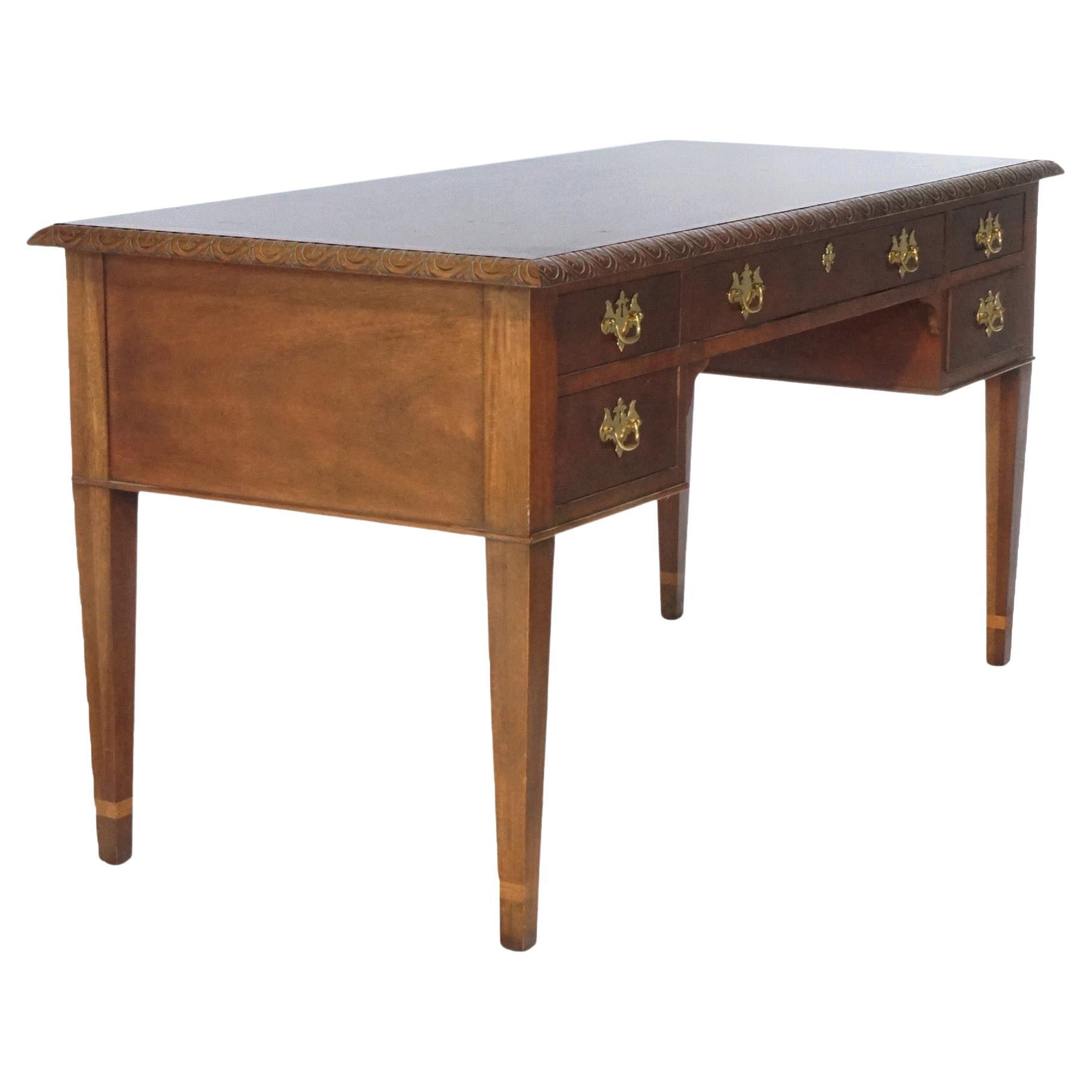 A Hepplewhite style kneehole desk of the Historic Charleston Collection by Baker offers mahogany construction with top having decorated trimming over single central drawer with flanking drawer towers, raised on straight and tapered legs with