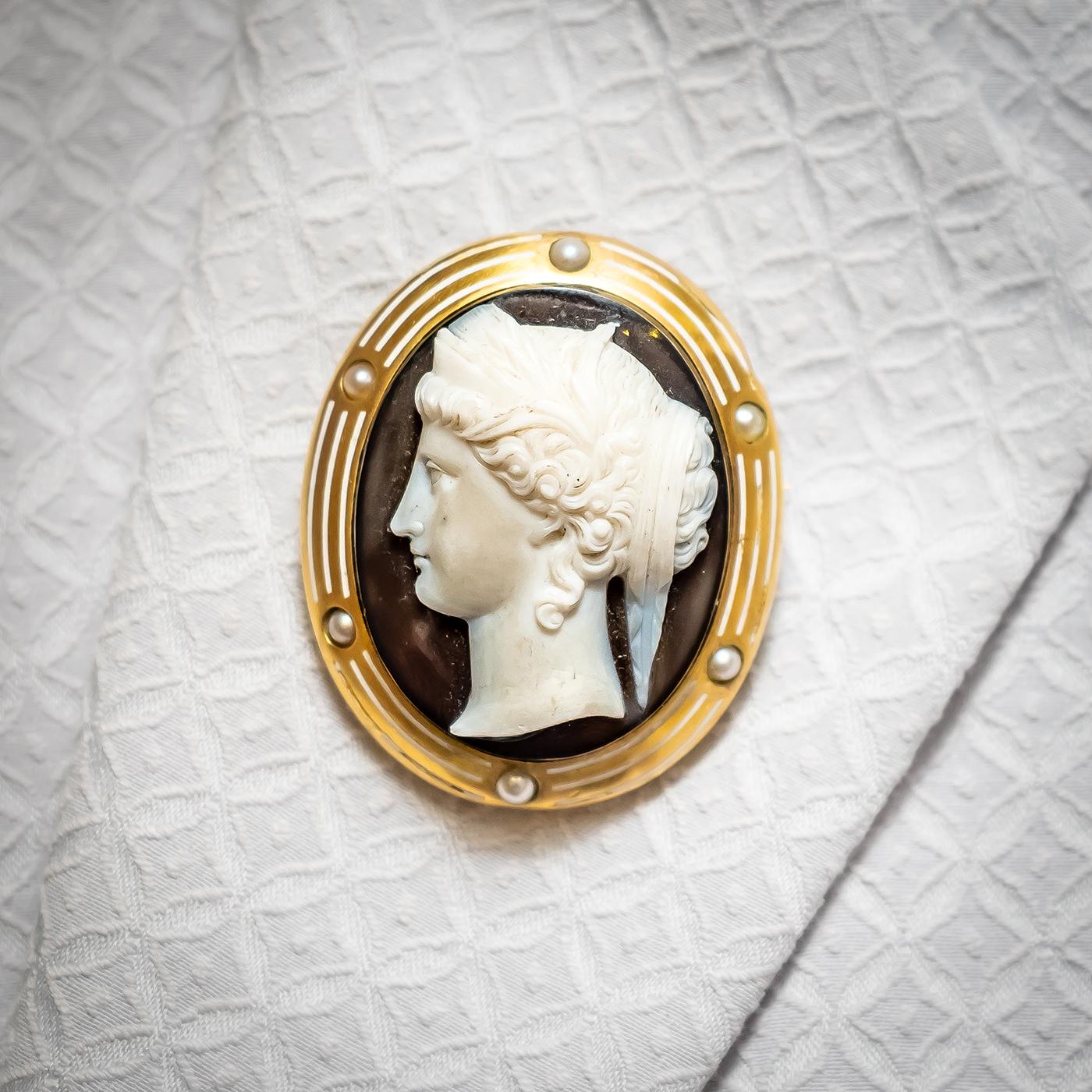 An antique cameo brooch, depicting Hera, the ancient Greek goddess of women, marriage and childbirth, on a sardonyx hardstone cameo, with a dark brown background, mounted in yellow gold surround, set with six, natural half pearls, spaced between