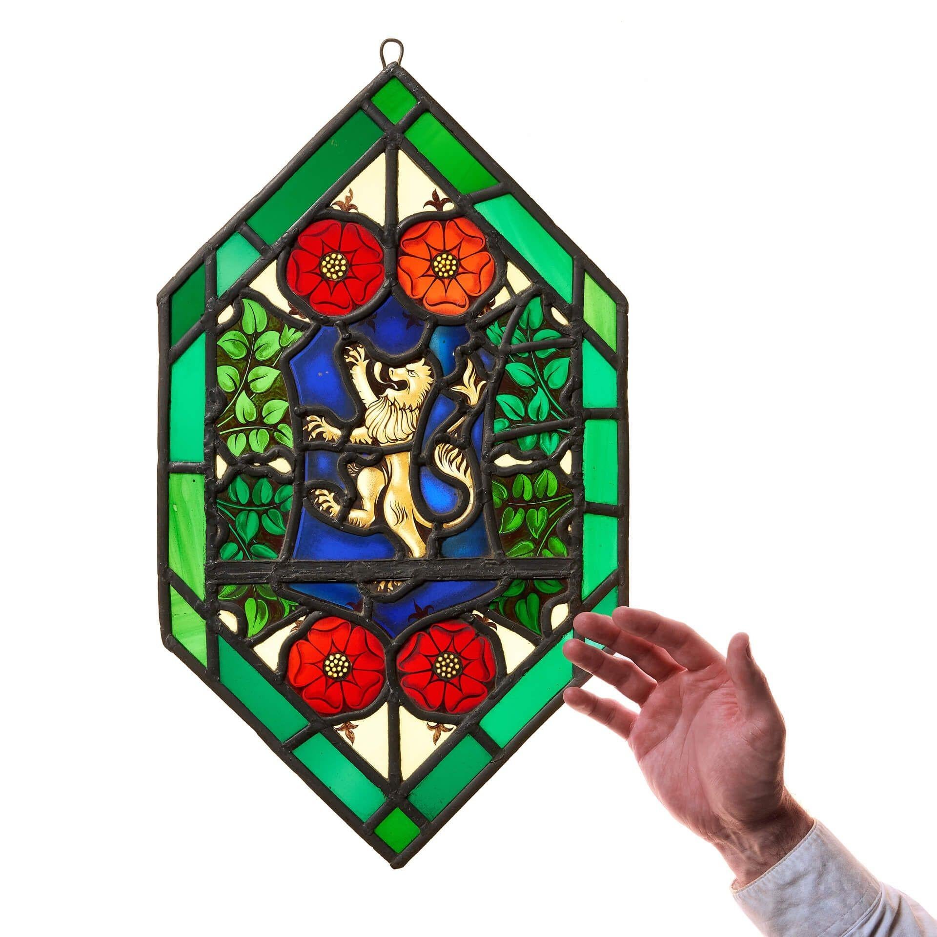 Un petit vitrail héraldique en forme de diamant, conçu de manière vibrante avec des vitres rouges, vertes et bleues. Bien que cette pièce date du début du 20e siècle, le style est beaucoup plus ancien, rappelant les fenêtres médiévales