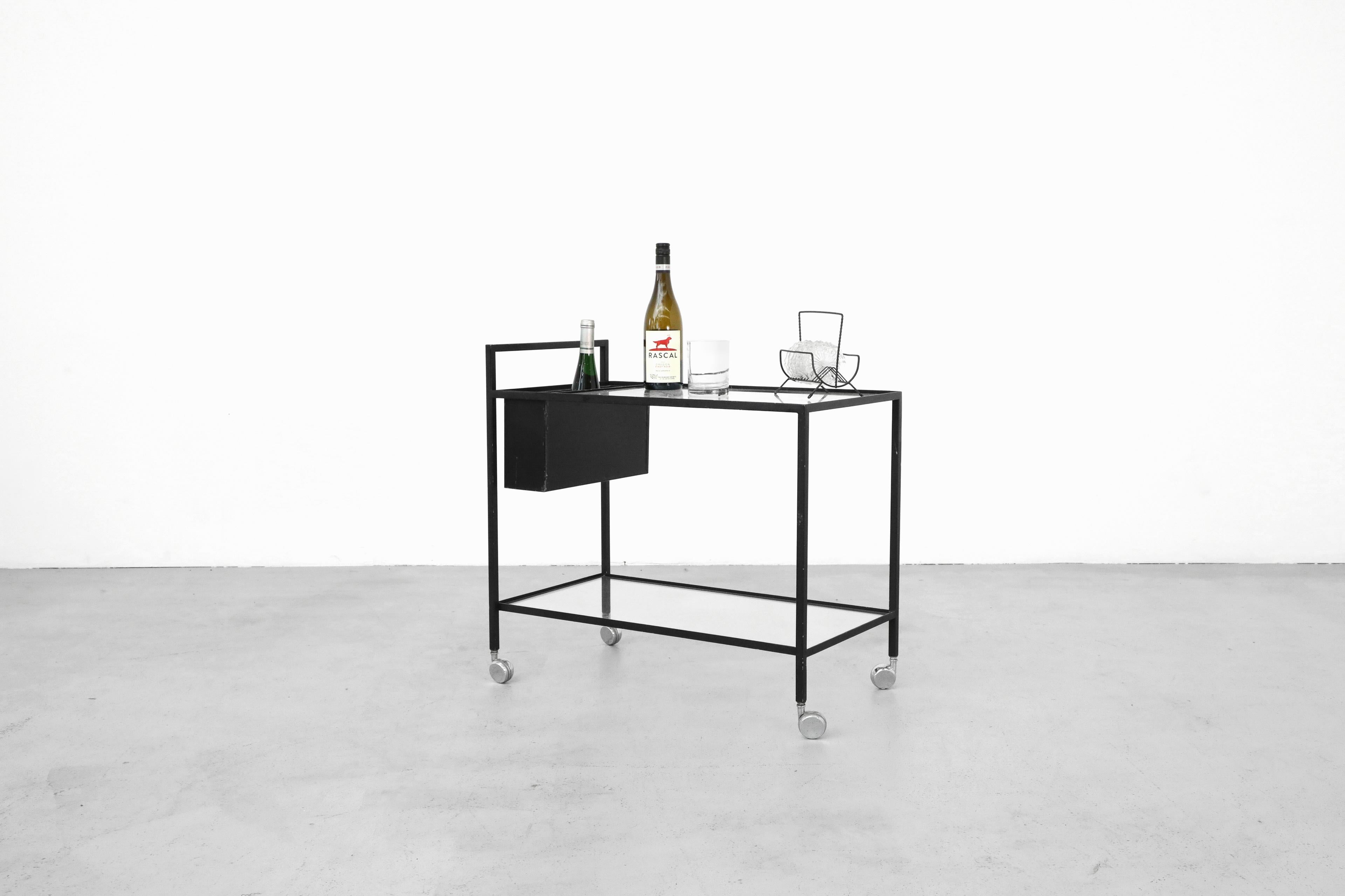 Herbert Hirch, influencé par le Bauhaus, chariot de bar roulant en métal émaillé noir avec porte-bouteilles en métal noir inséré qui peut être positionné à l'avant ou à l'arrière du chariot. Les tablettes en verre sont encastrées dans le cadre pour