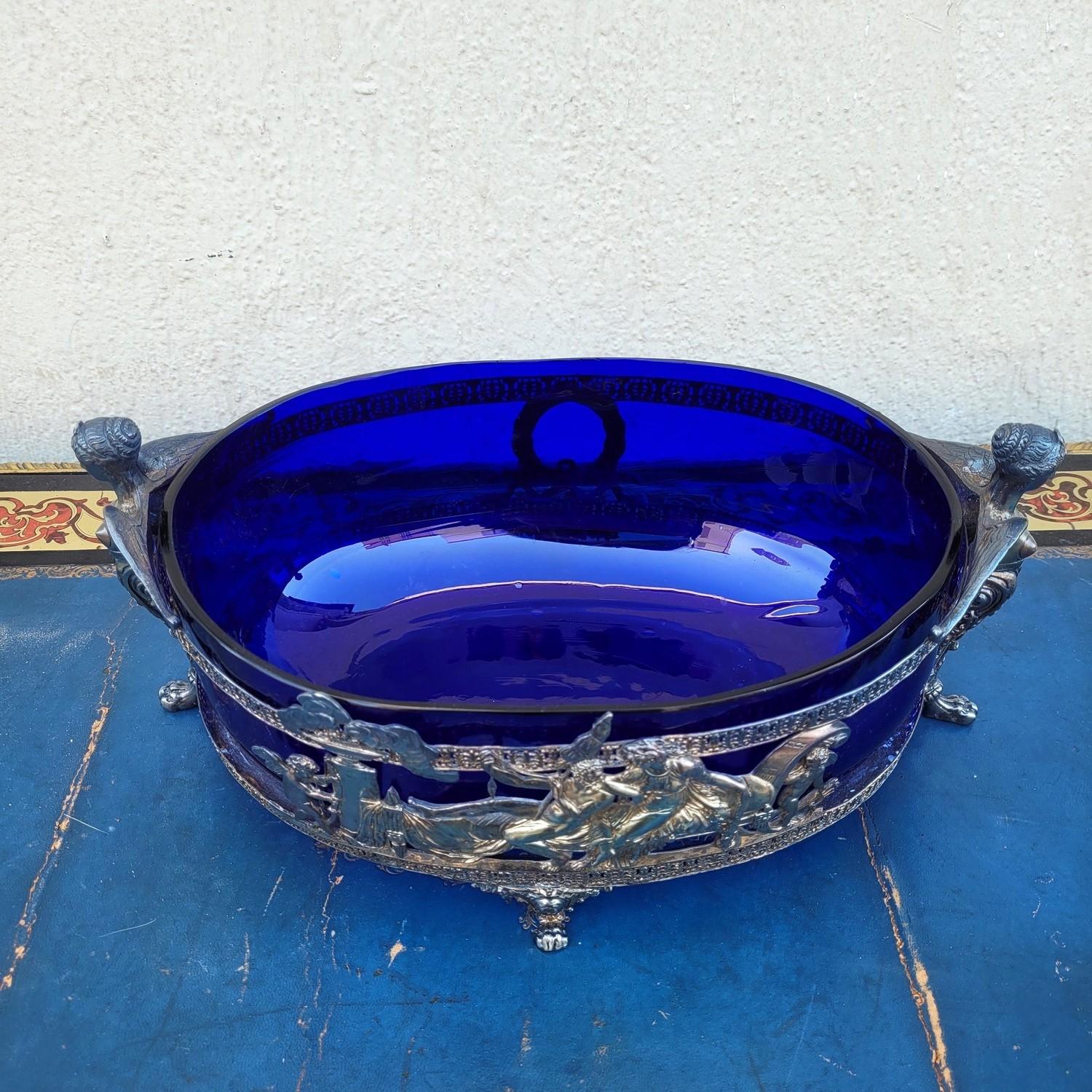 Blue glass Bowl, set in a silver-plated metal frame: the decoration represents Hercules and Omphale on one side: Hercules spins wool and Omphale has taken on the attributes of the lion skin and the club.
On each side, a winged caryatid with lion's