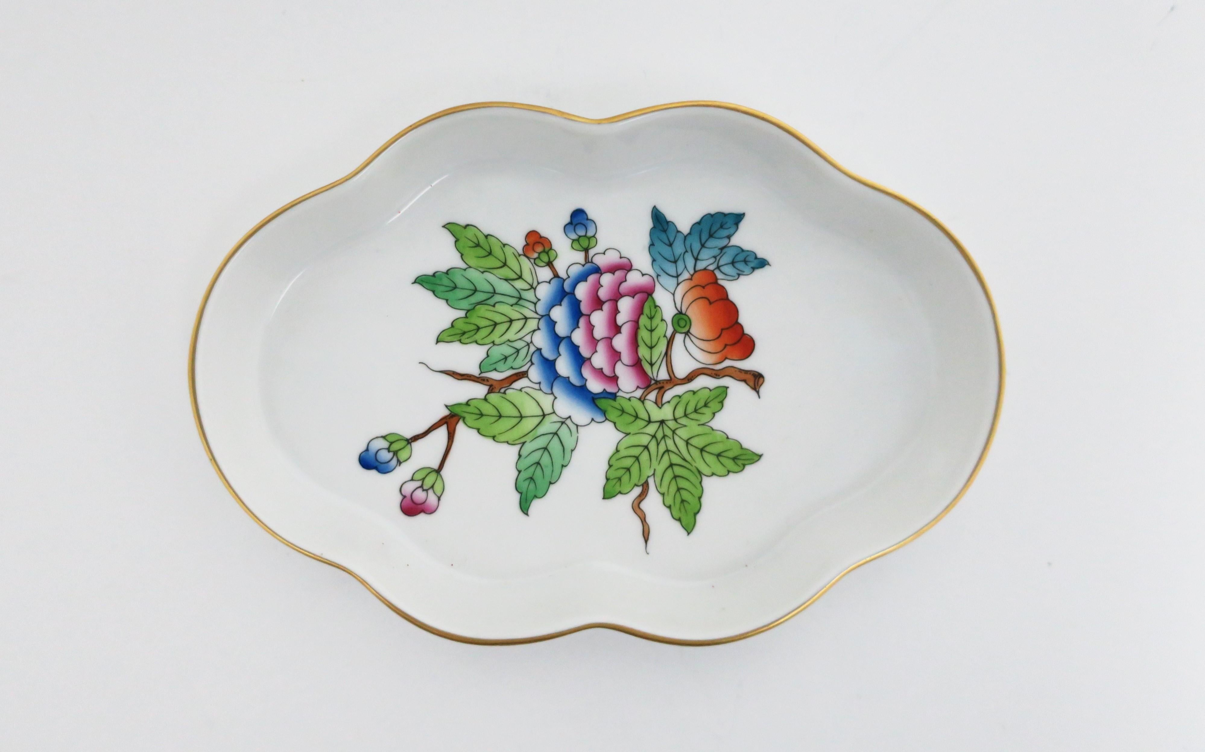 A beautiful vintage Herend white porcelain jewelry dish, circa 20th century, Hungary. A beautiful oval piece with colorful flower and leaf design at center and a scalloped edge finished with gold detail. Colors are vibrant; greens, blues, pinks, and