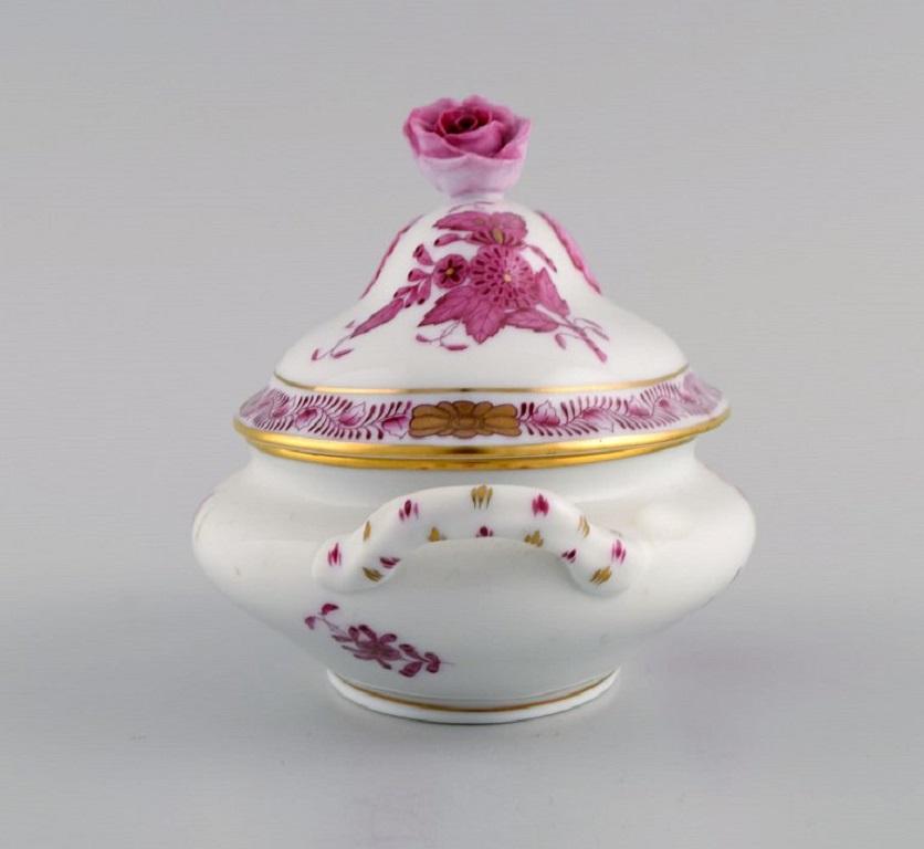 Herend lidded trinket box in porcelain with hand-painted purple flowers and gold decoration. Lid modelled with a rose bud. 
Mid-20th century.
Measures: 14 x 9.5 cm.
In excellent condition.
Stamped.