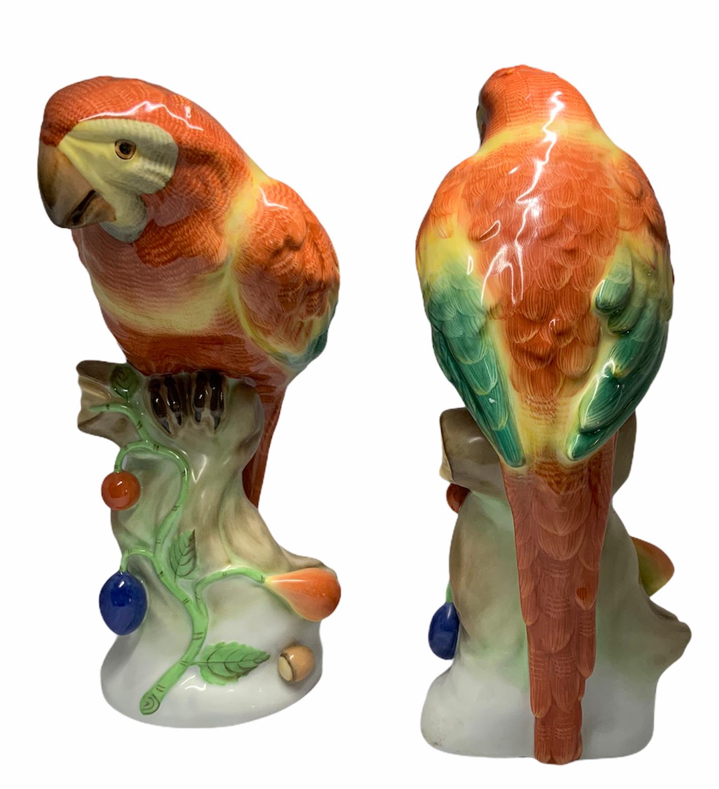 This is a pair of hand painted parrots in tropical colors of orange,green & yellow. They are standing over a wood branches that have some vines with fruits hanging from it. Under the base is the Herend hallmark.