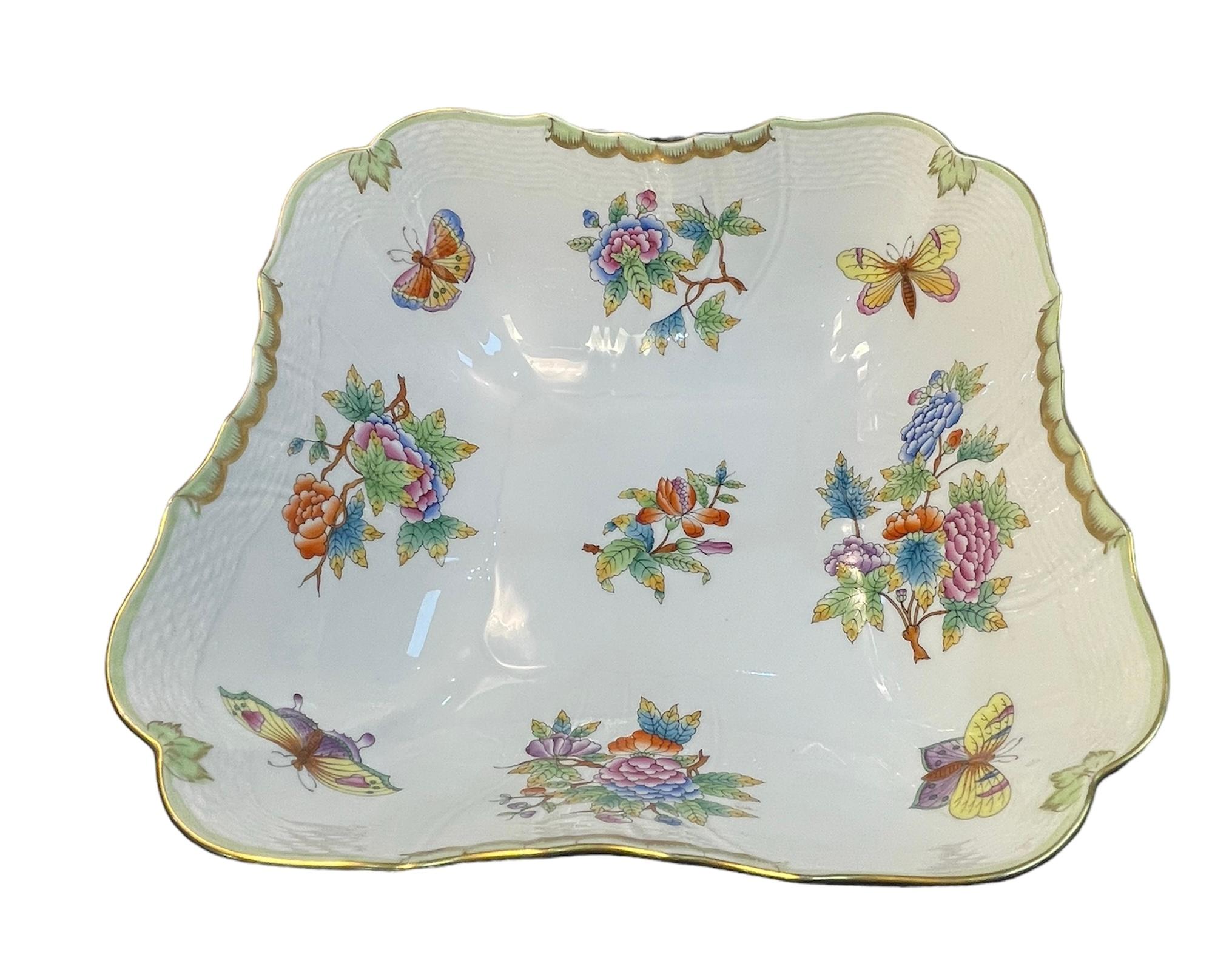This is a Herend Porcelain Queen Victoria Pattern Salad Bowl. It depicts a square bowl decorated with colorful small bouquets of flowers and butterflies. The scalloped border is hand painted mint green color. It is enhanced by a gilt swag in some