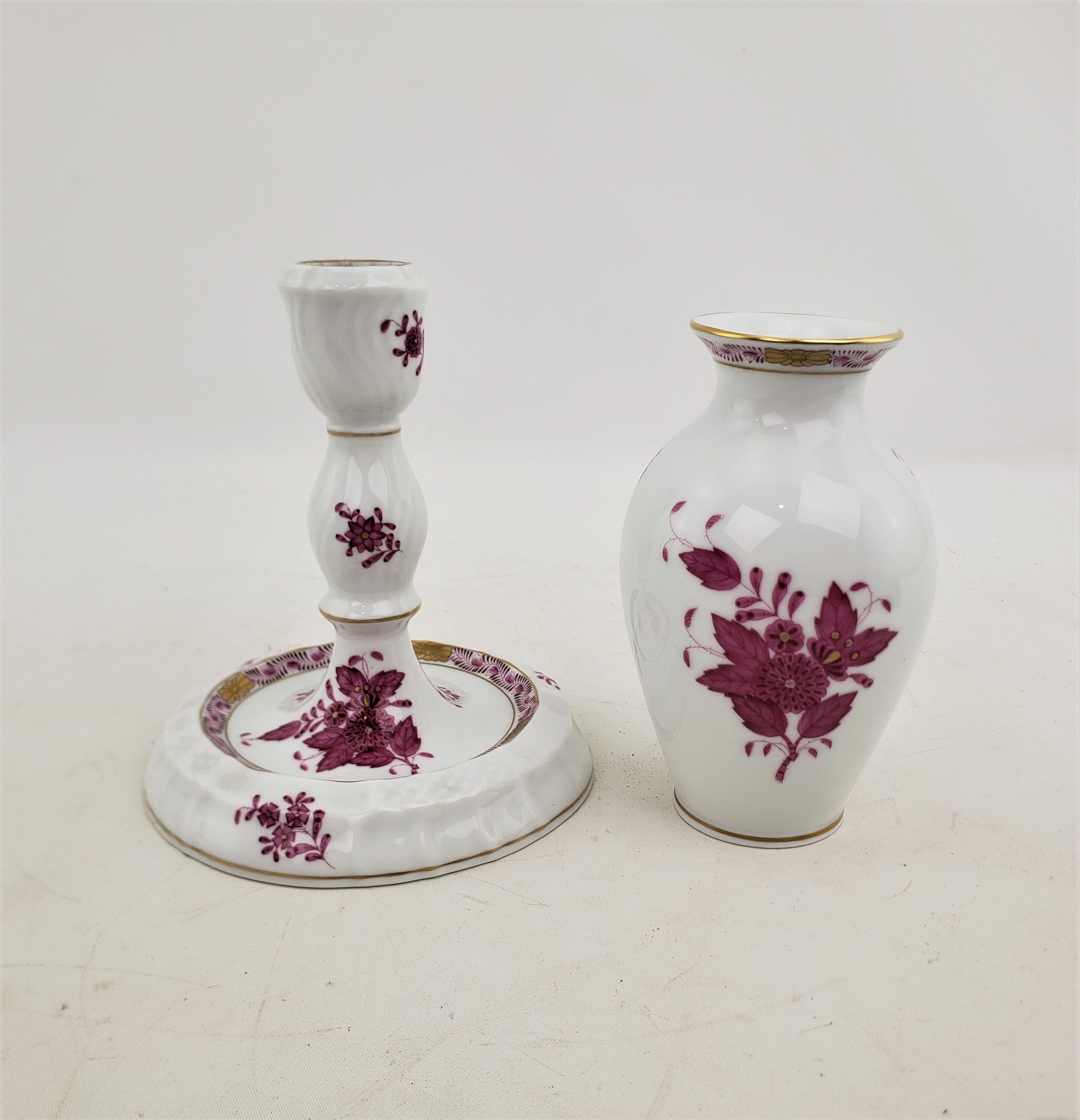 This candlestick and vase were made by the well known Herend factory of Hungary in approximately 1970 in their signature Chinaoserie style. The pair is composed of porcelain with hand painted decoration in their Chinese Bouquet pattern in a